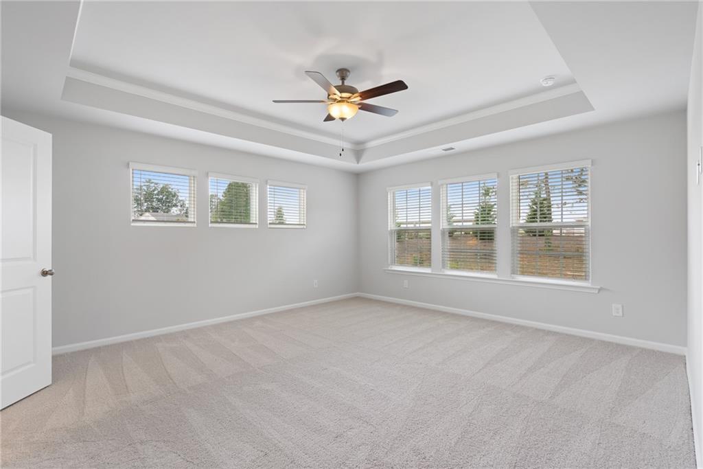 Bright upstairs bonus room with tray ceiling, ceiling fan, and large triple windows in Davidson Homes The Hickory A, Winder, GA