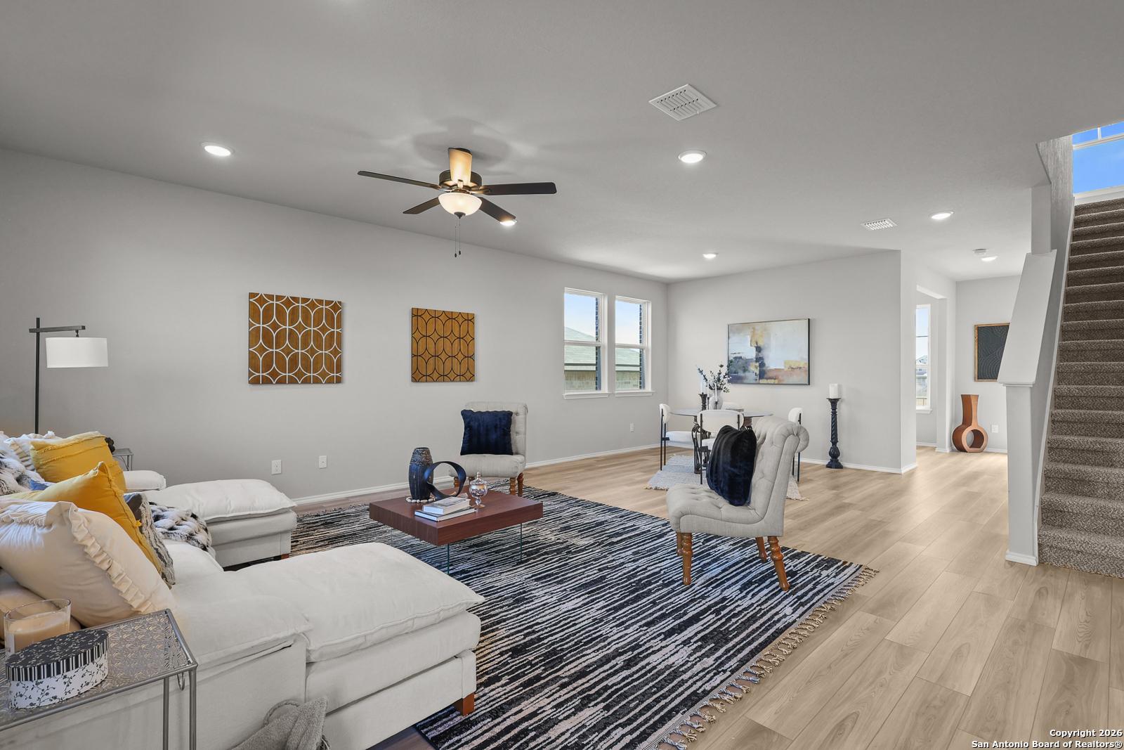 Modern living room with white sectional sofa, ceiling fan, open staircase, and artwork in Davidson Homes The Murray K, San Antonio, Texas