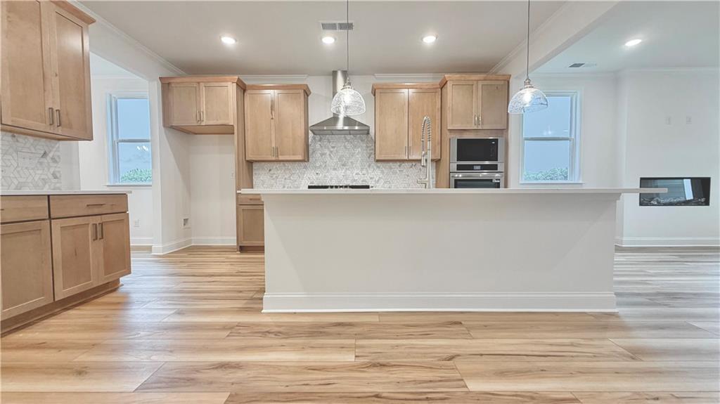 Modern kitchen with light wood cabinets, kitchen island, and stainless appliances in The Glenwood A at Wehunt Meadows, Hoschton