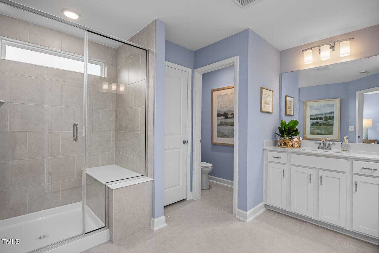 Modern master bathroom with frameless glass shower, blue walls, dual sink vanity, and artwork in Davidson Homes The Graham, Fuquay-Varina, NC