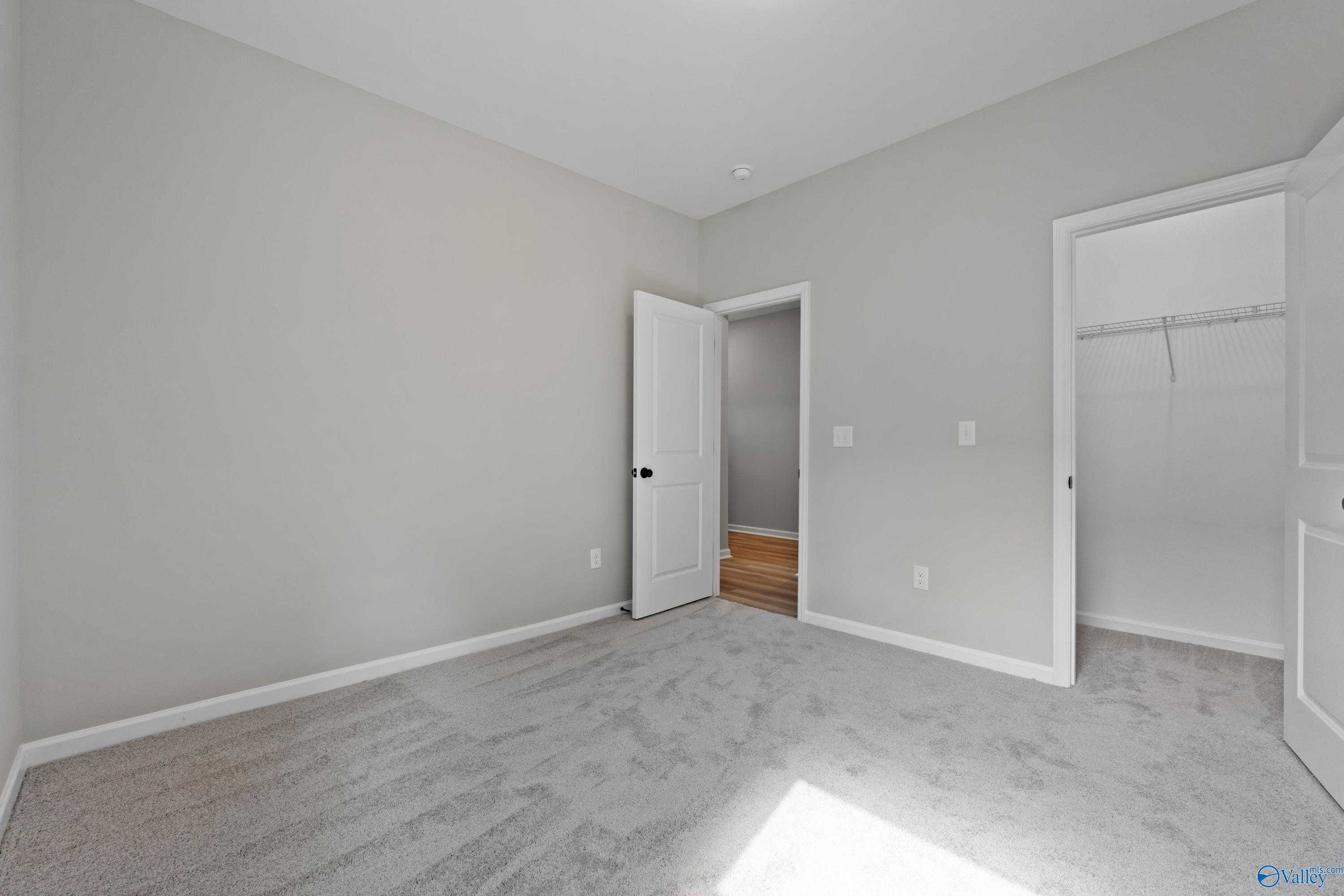 Cozy bedroom with light gray walls, plush carpet, open door to bathroom, and built-in closet in Davidson Homes The Phoenix, Fayetteville, TN
