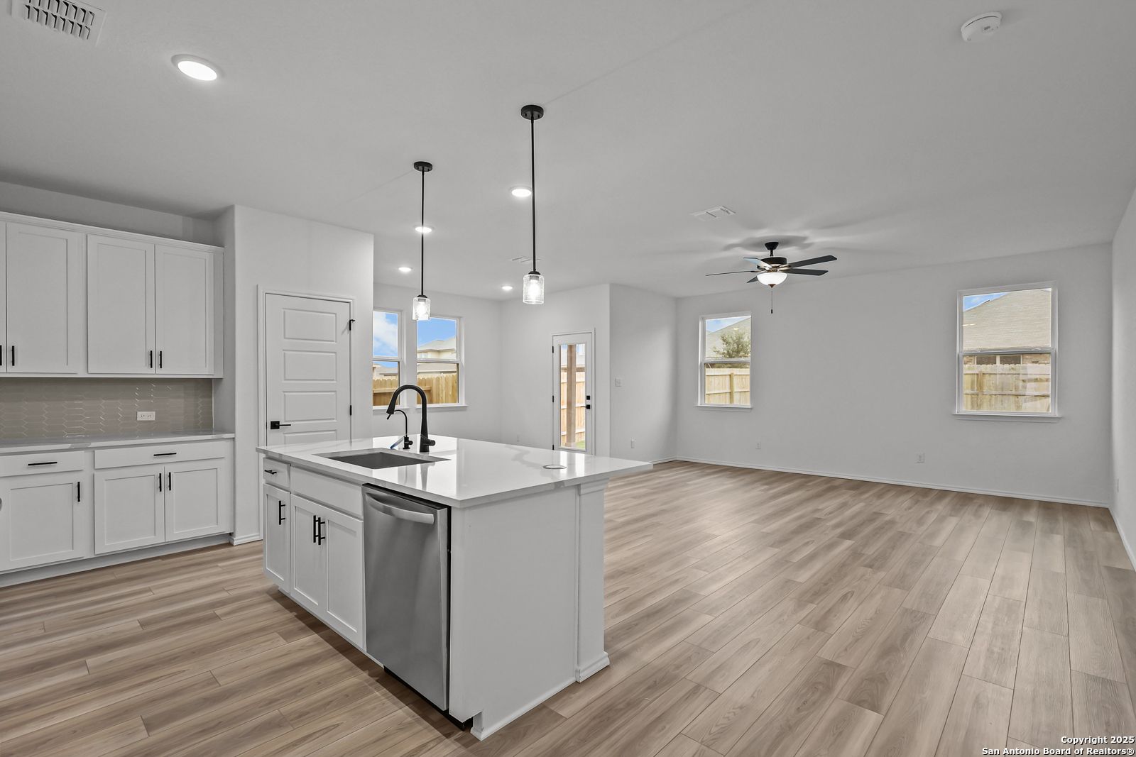 Modern open-concept kitchen with white shaker cabinets, quartz island, stainless sink, and pendant lights in The Daphne J home, Converse, Texas