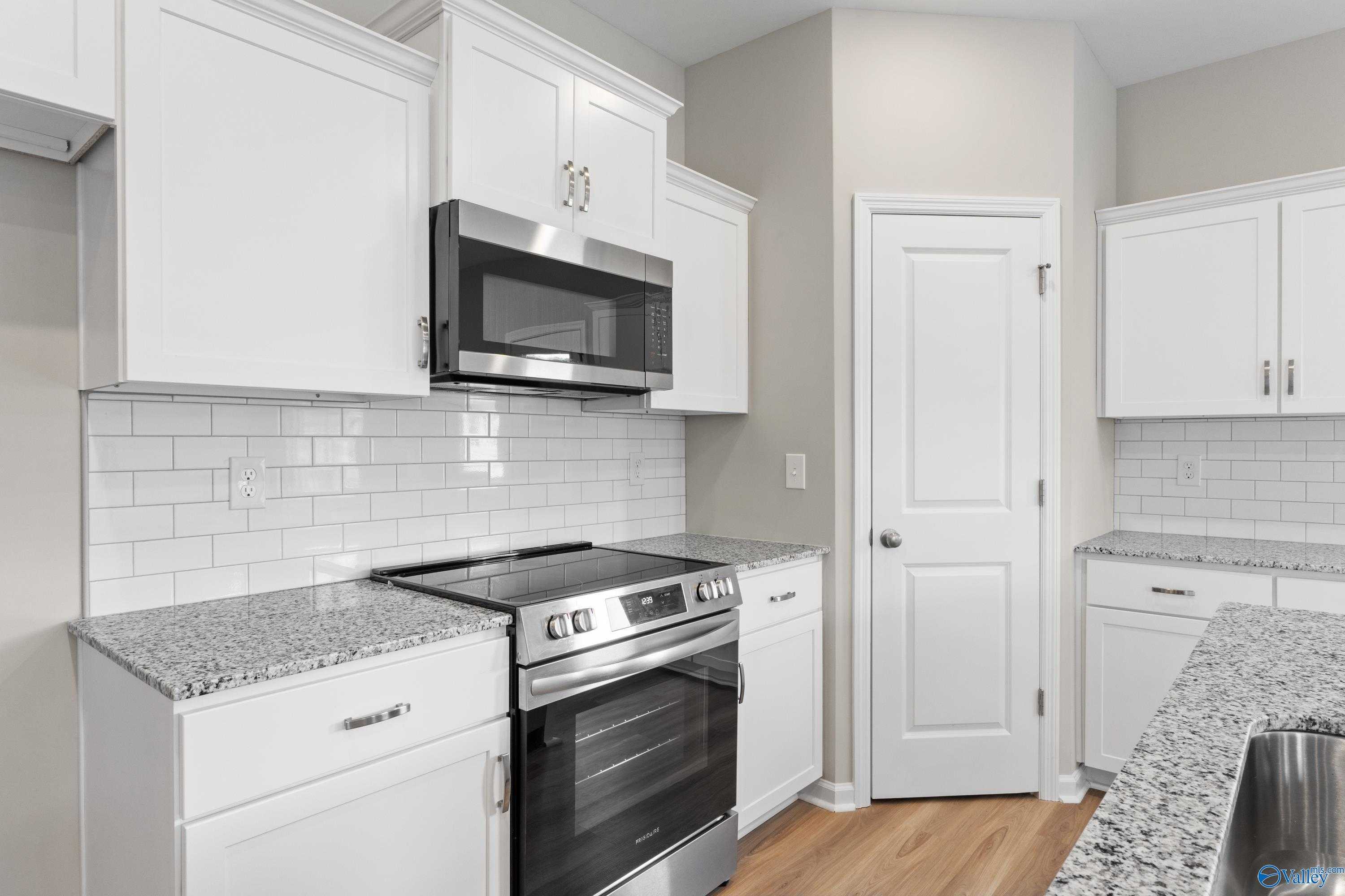 Modern kitchen with white shaker cabinets, speckled granite counters, stainless steel oven and microwave in Evermore Homes The Augusta, Madison AL