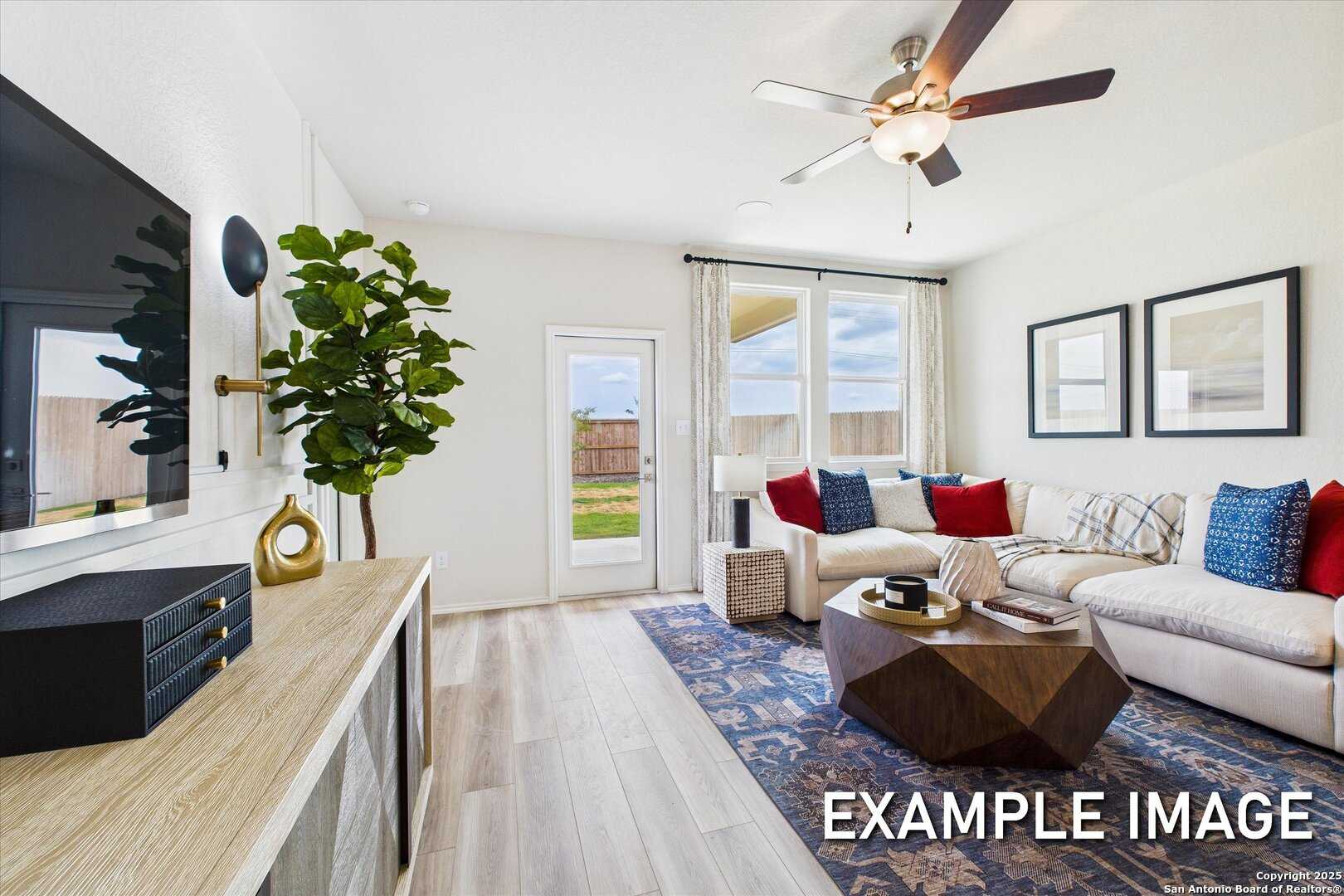 Cozy living room with white L-shaped sofa, geometric coffee table, wall-mounted TV, French doors to backyard, and ceiling fan in Davidson Homes Brazos C, San Antonio