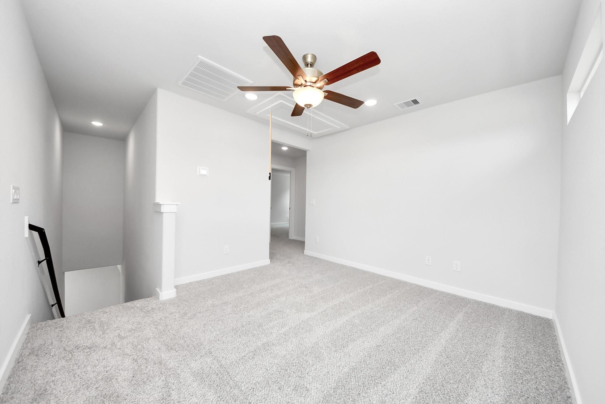 Spacious carpeted game room with ceiling fan in The Sabine E floor plan at Windmill Estates, Magnolia, Texas.