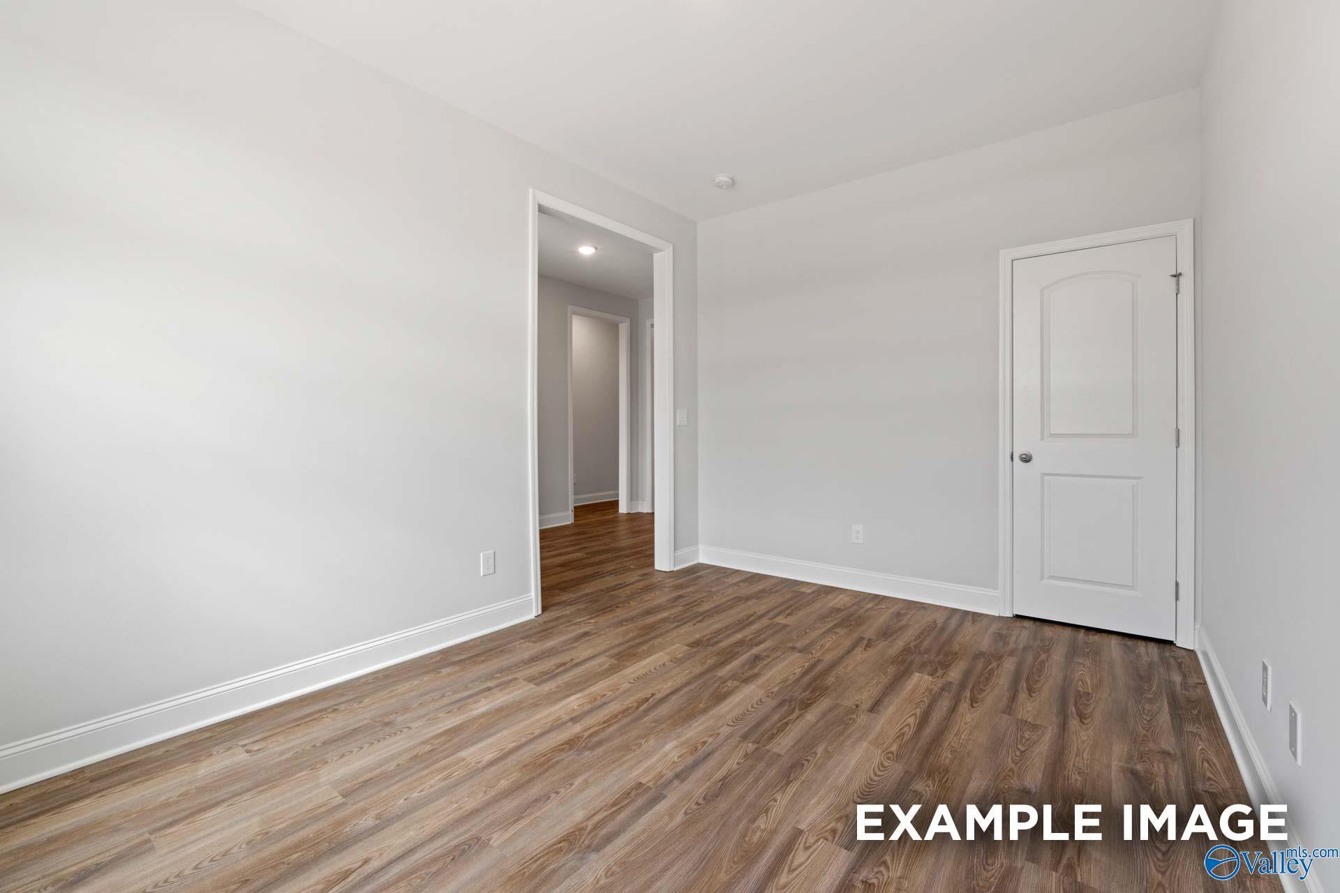 Bright empty bedroom with light hardwood floors, white walls, and open hallway door in Davidson Homes The Harrison B, Toney, Alabama