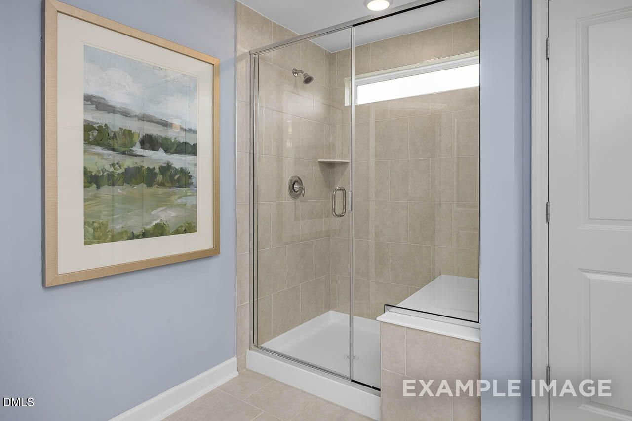 Modern master bathroom with frameless glass shower, beige tile bench, clerestory window, and abstract art in Davidson Homes The Graham, Fuquay-Varina