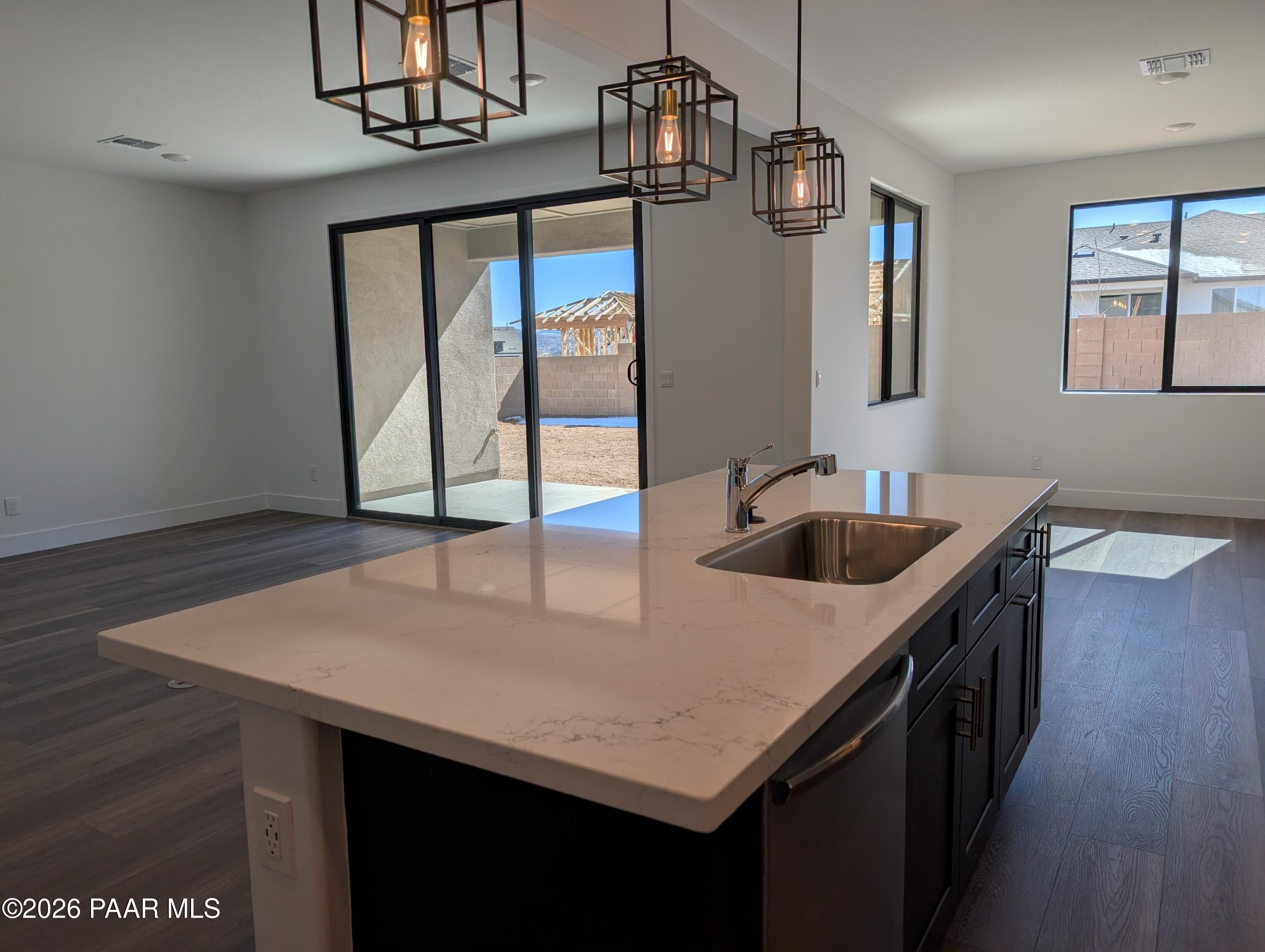 Modern kitchen island with white quartz countertop, stainless sink, black cabinets, and sliding doors to desert patio in Prescott, Arizona home