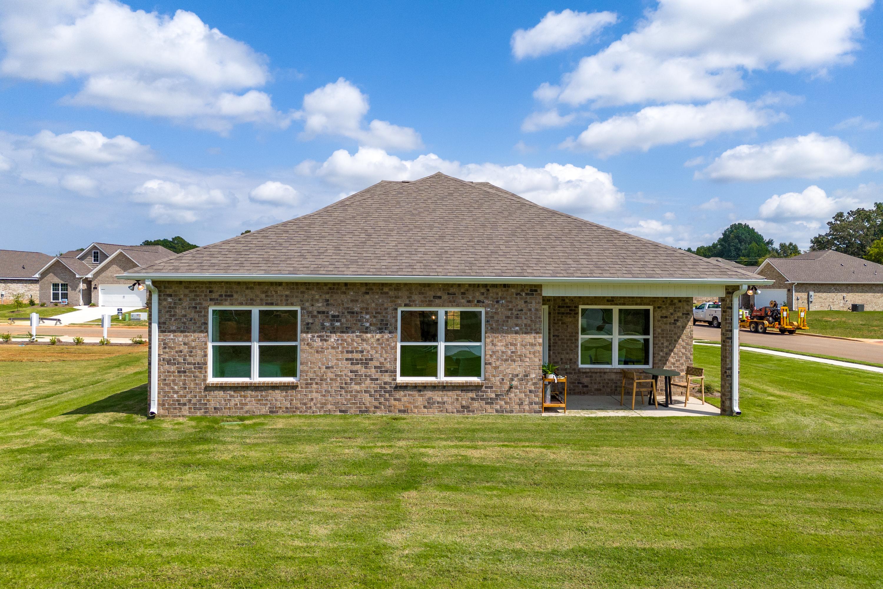 Brick home side view at Wood Trail in Toney Alabama featuring covered patio with seating and lush green lawn