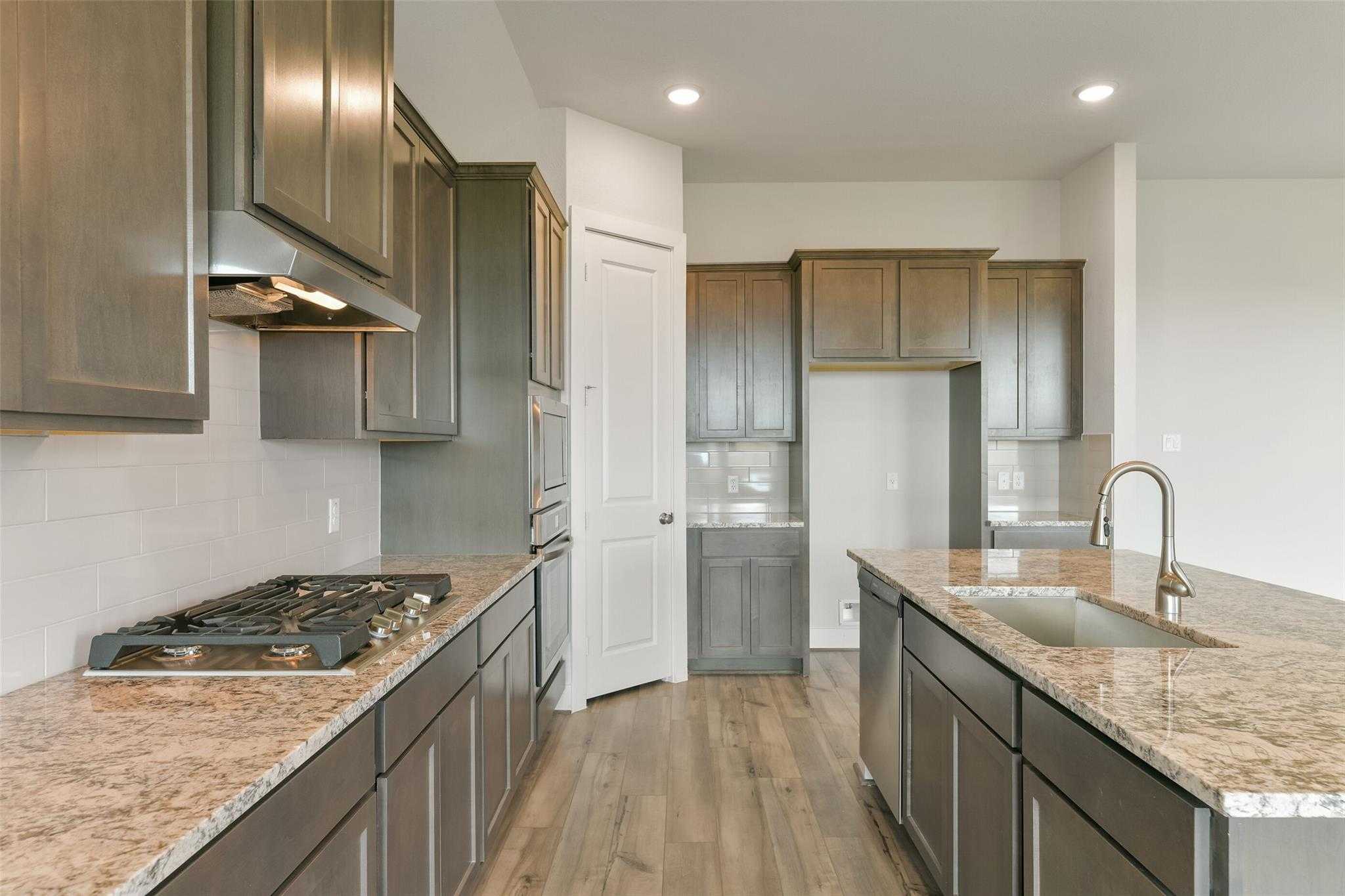 Modern kitchen featuring granite island, stainless appliances, dark shaker cabinets in Davidson Homes The Edward A, Lago Mar, Texas City