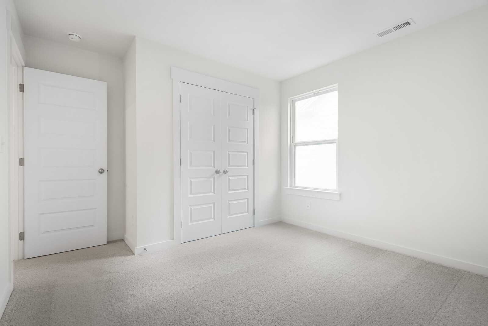 Empty secondary bedroom featuring double closet doors, window, and neutral carpet in Davidson Homes The Logan C, Gallatin, TN