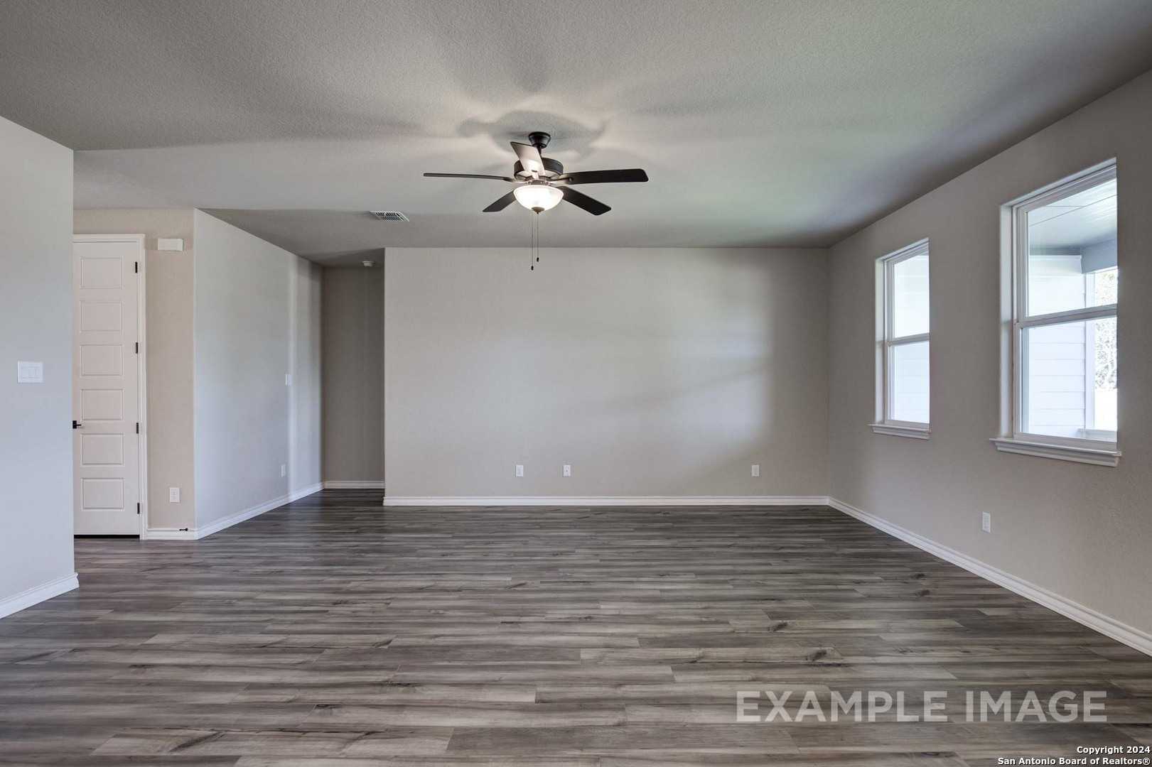 Spacious empty living room with ceiling fan, large windows, and gray laminate flooring in Davidson Homes Rockford G, San Antonio