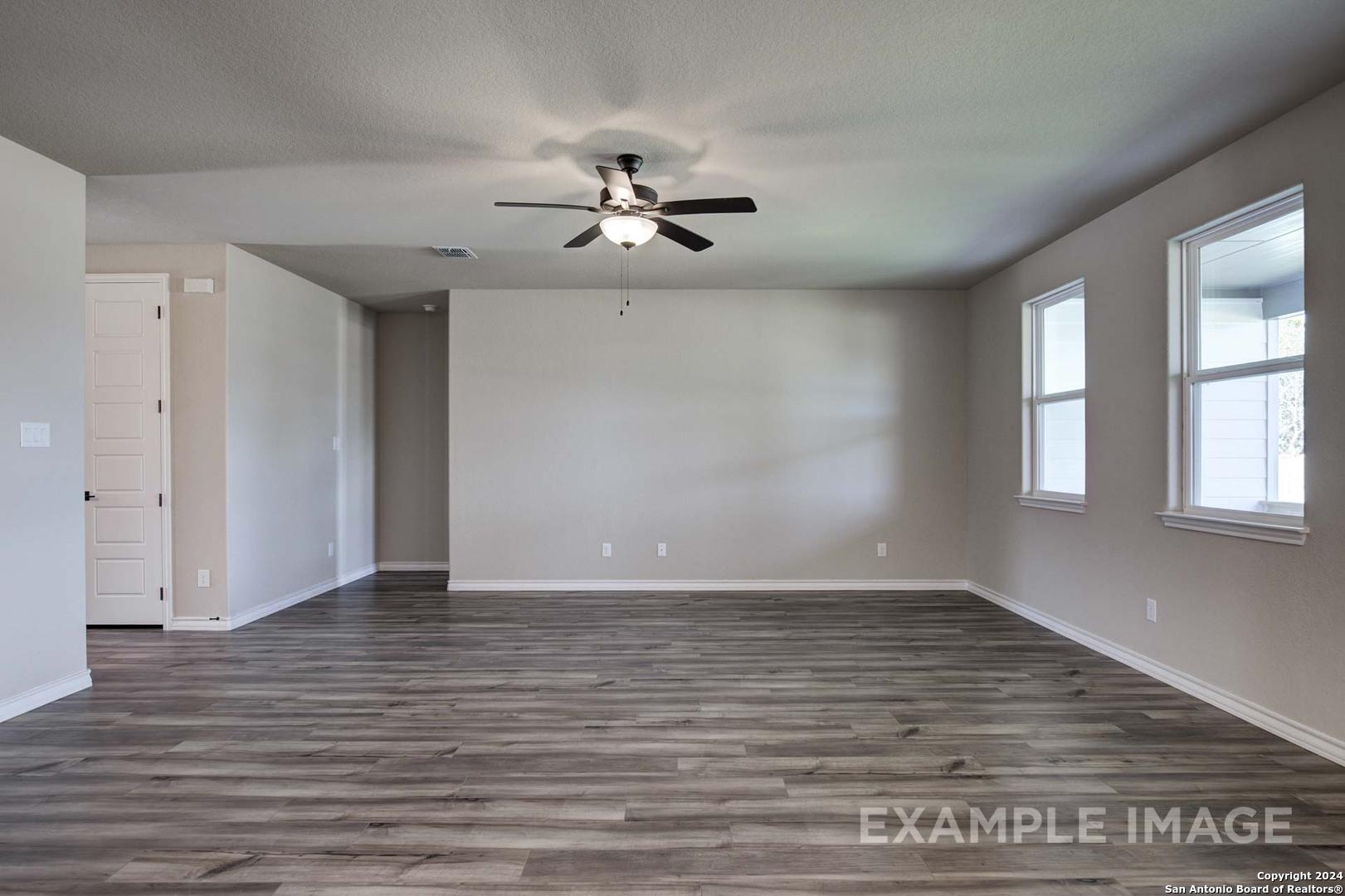 Spacious empty living room with ceiling fan, large windows, and gray laminate flooring in Davidson Homes Rockford G, San Antonio