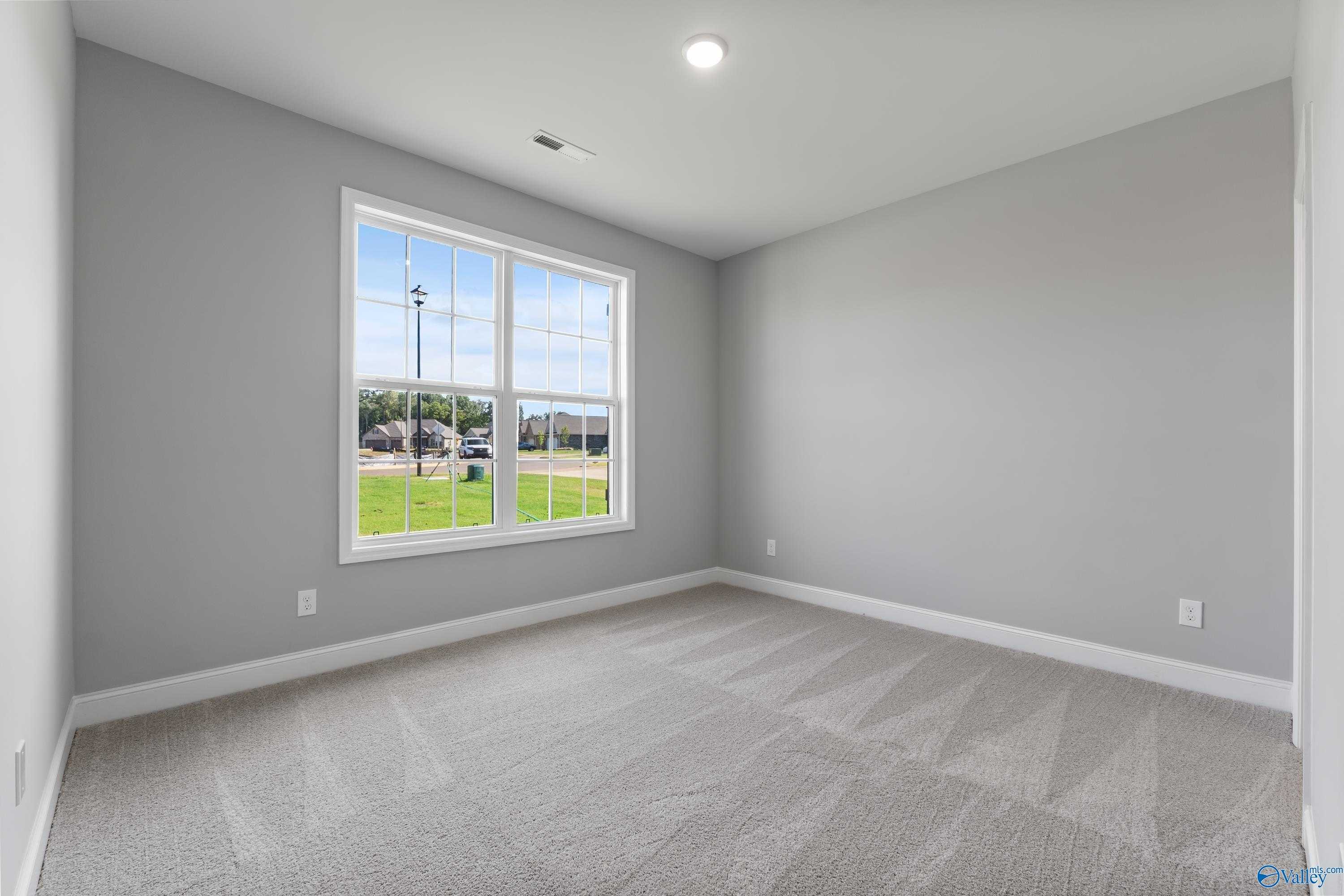Bright secondary bedroom with gray walls, carpeted floor, and large window view of green field in Davidson Homes The Rockford, Harvest, AL