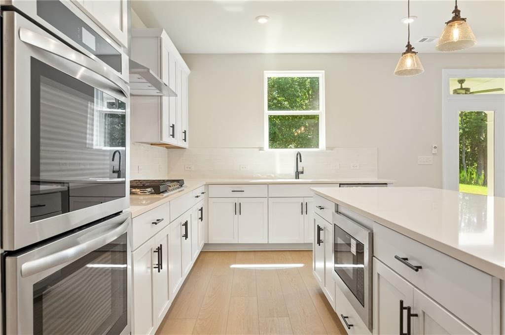 Bright U-shaped kitchen with white shaker cabinets, quartz island, stainless double ovens in The Hickory E home, Buford, GA