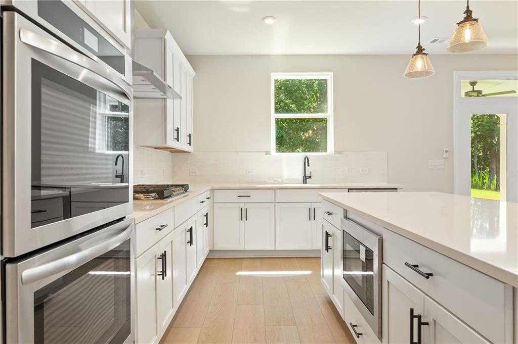 Modern white U-shaped kitchen with stainless double ovens, quartz island, and backyard view in The Hickory E, Buford, GA