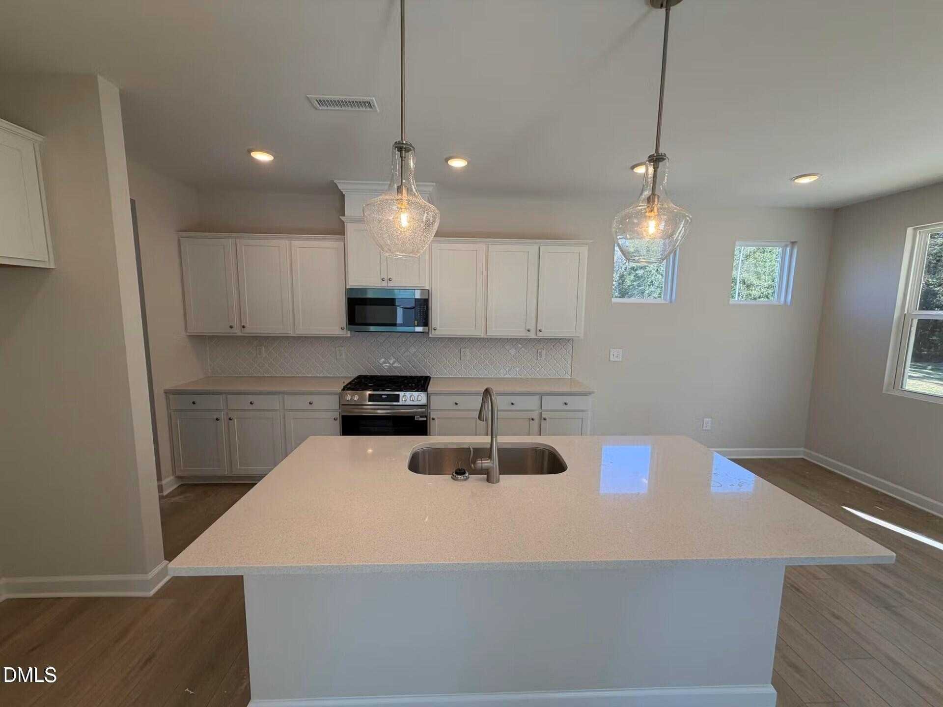 Modern white kitchen with quartz island, farmhouse sink, stainless appliances, and pendant lights in Davidson Homes The Gavin C, Lillington, NC