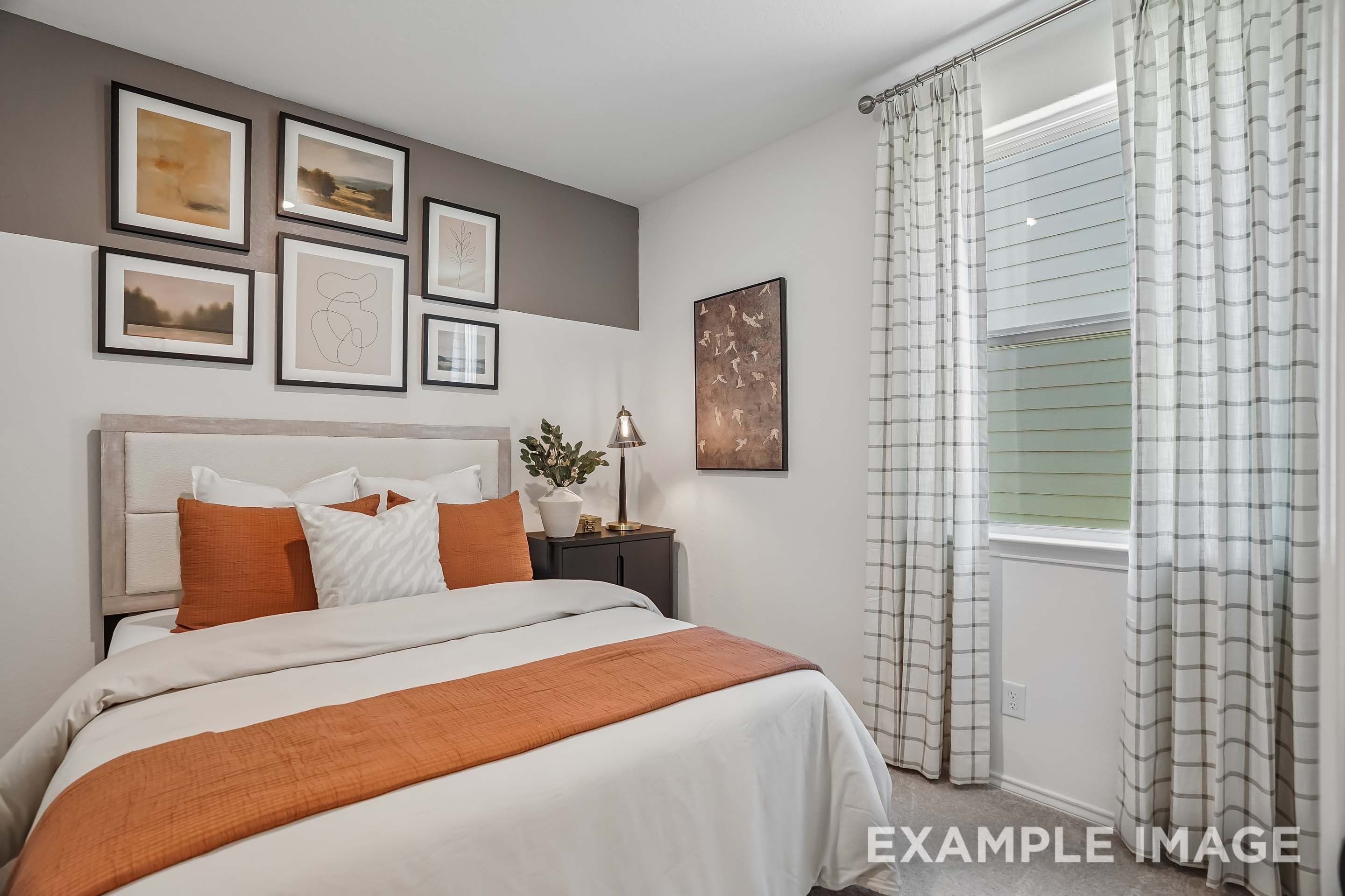 Cozy bedroom in The Pinecrest D floor plan featuring modern decor, gallery wall art, and burnt orange bedding accents.