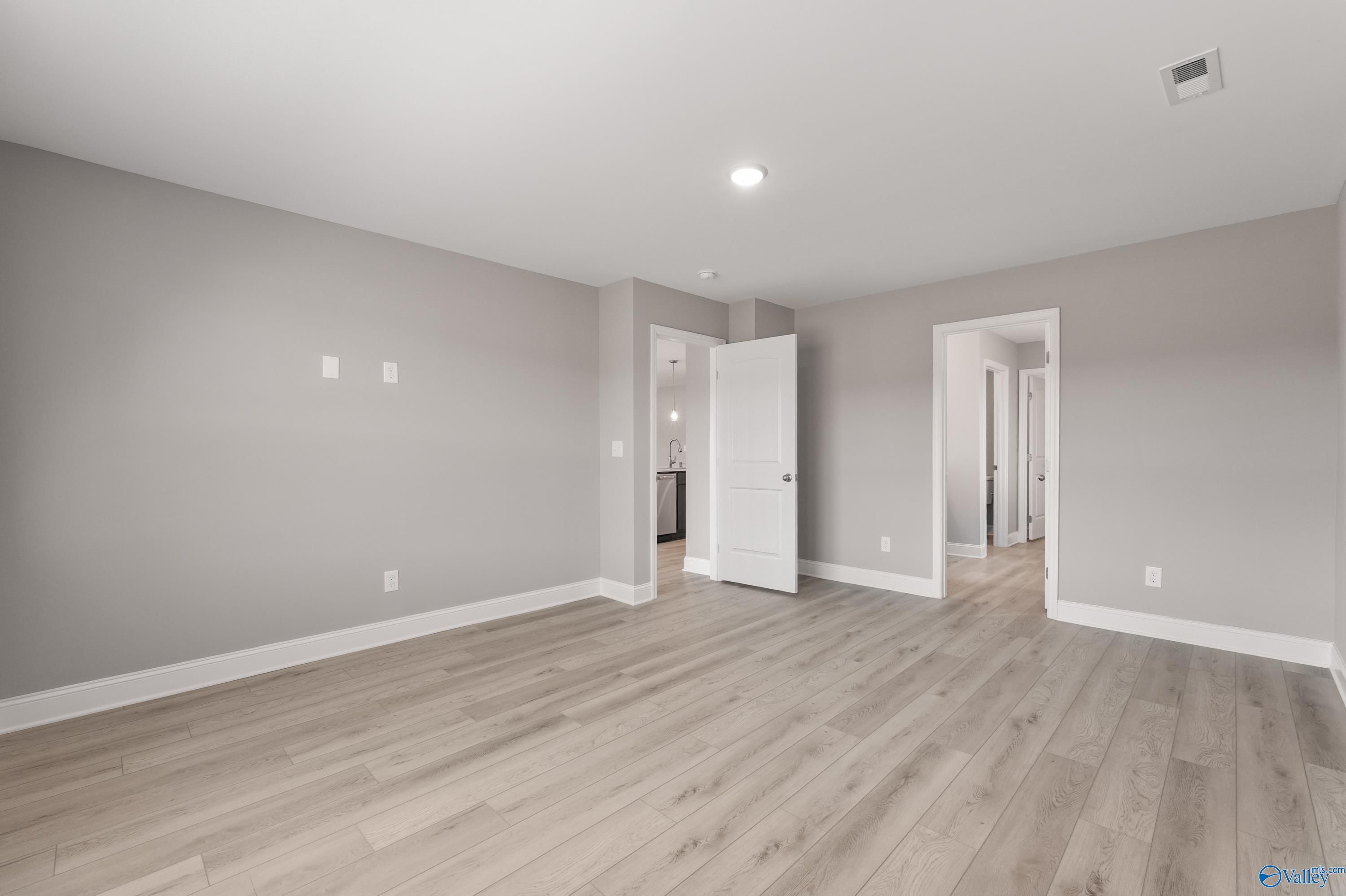 Spacious empty room with light gray walls, light wood laminate floors, and open doorways in Davidson Homes The Everett B, Athens, Alabama