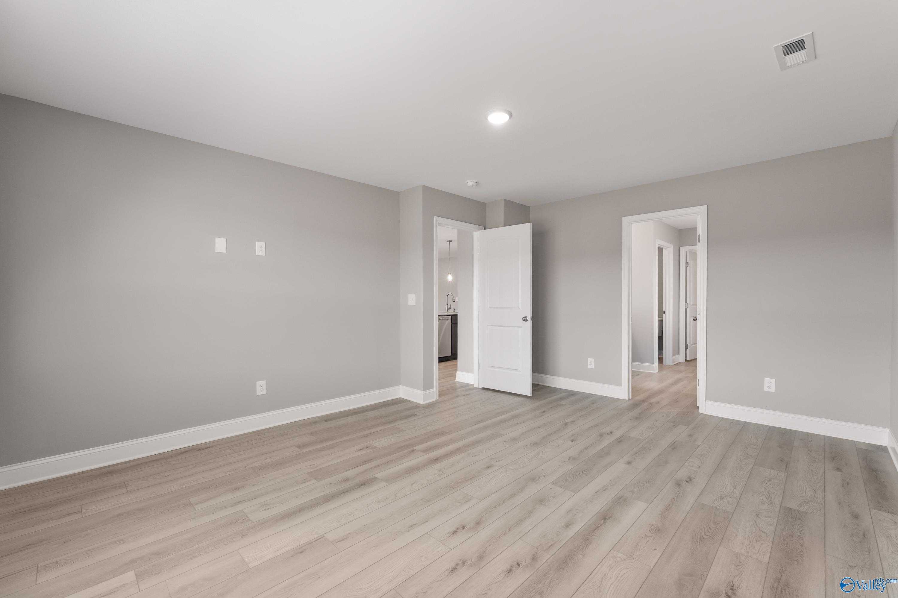 Spacious interior hallway with gray walls, light wood floors, and open doorways in The Everett B 4-bedroom home, Athens, Alabama