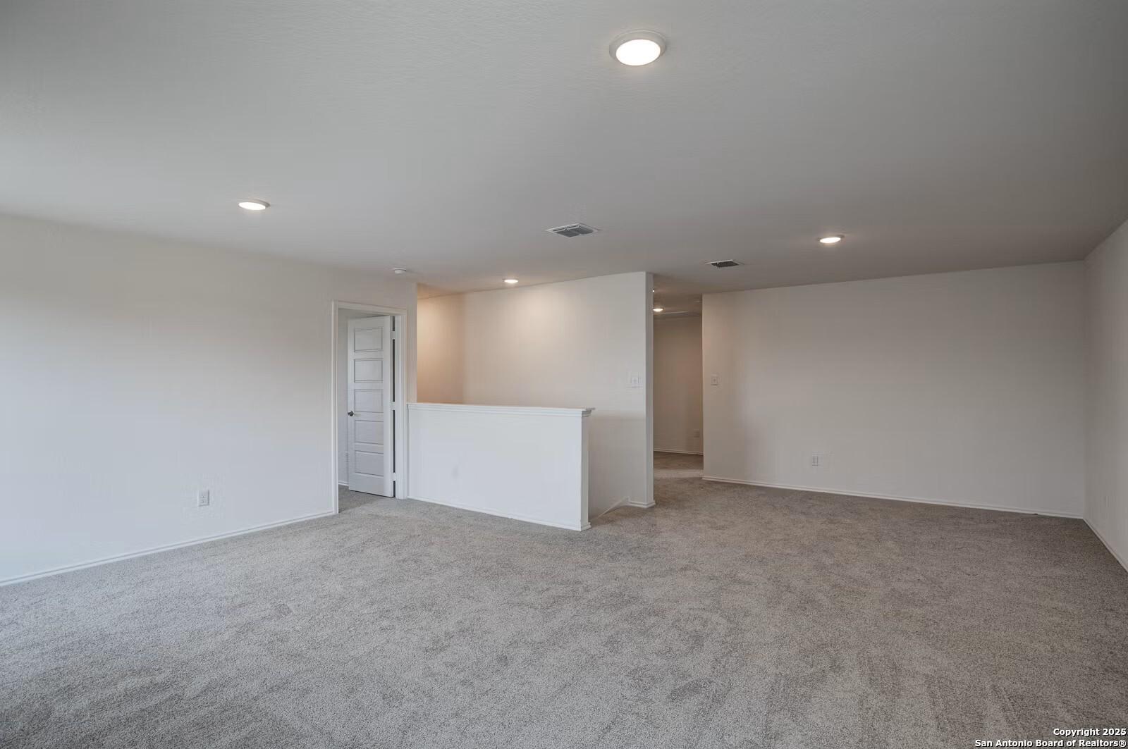 Spacious upstairs hallway with beige carpet, white walls, recessed lights, and balcony overlook in Davidson Homes The Douglas B, Seguin, Texas