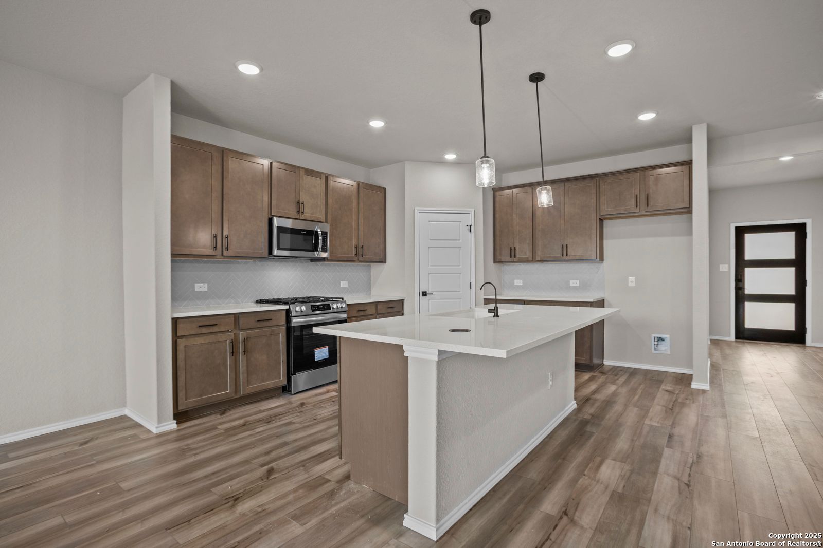 Modern kitchen with wood cabinets, quartz island, stainless appliances, and pendant lights in Davidson Homes The Douglas F, San Antonio