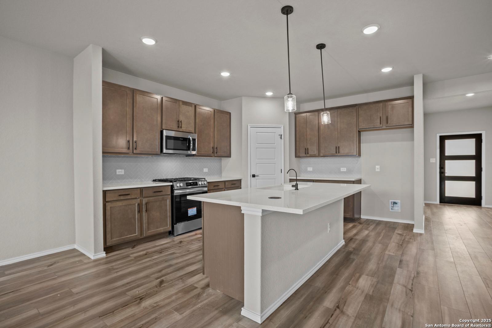 Modern kitchen with wood cabinets, quartz island, stainless appliances, and pendant lights in Davidson Homes The Douglas F, San Antonio