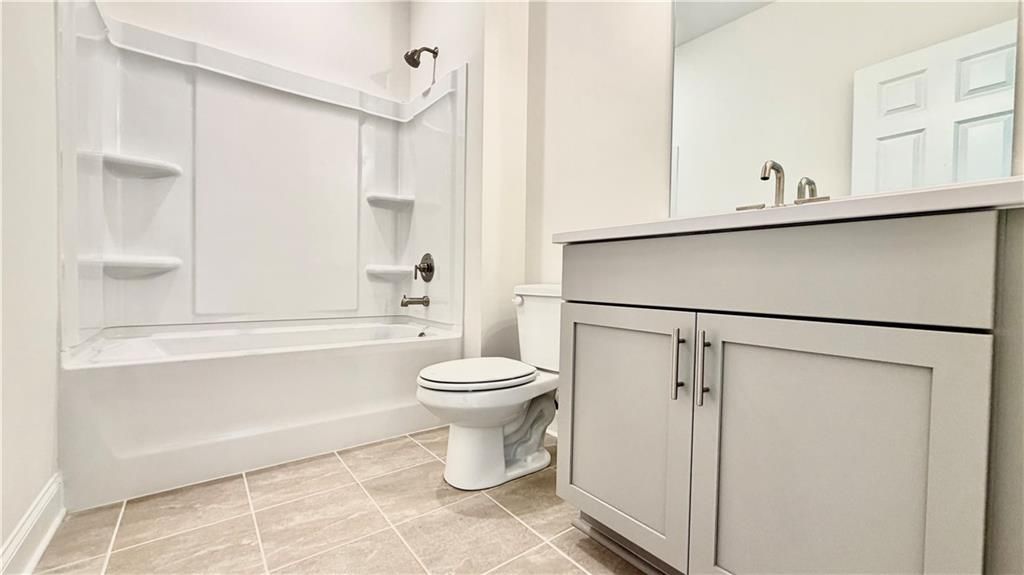 Modern bathroom with white tub-shower combo and gray vanity in The Hickory C floor plan at Wehunt Meadows, Hoschton, GA.