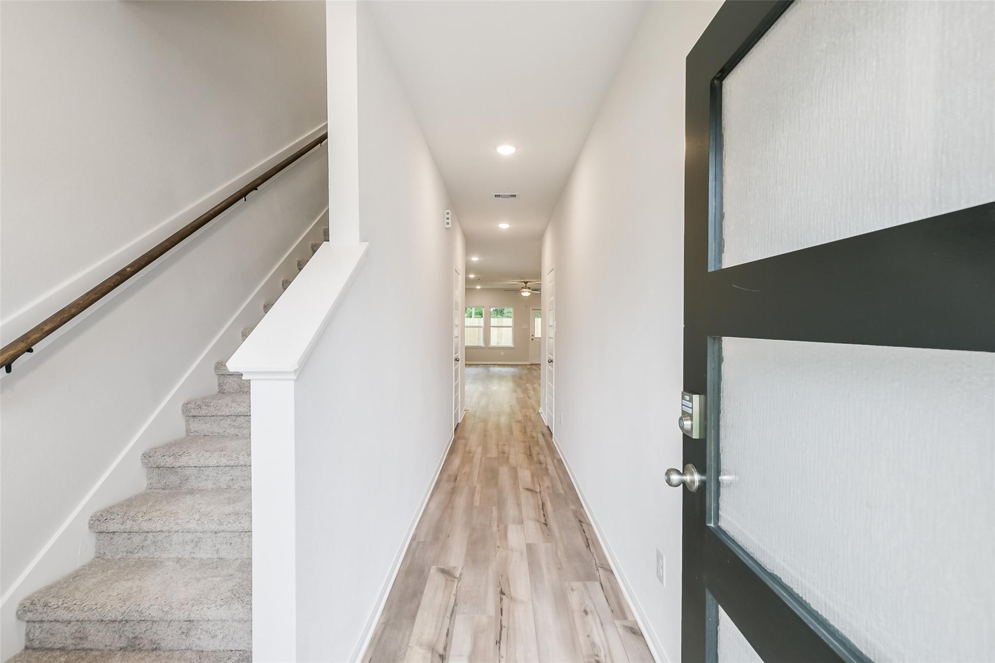 Spacious entry hallway with light oak floors, white walls, carpeted staircase, and black glass front door in Davidson Homes The Brazos F, Conroe TX