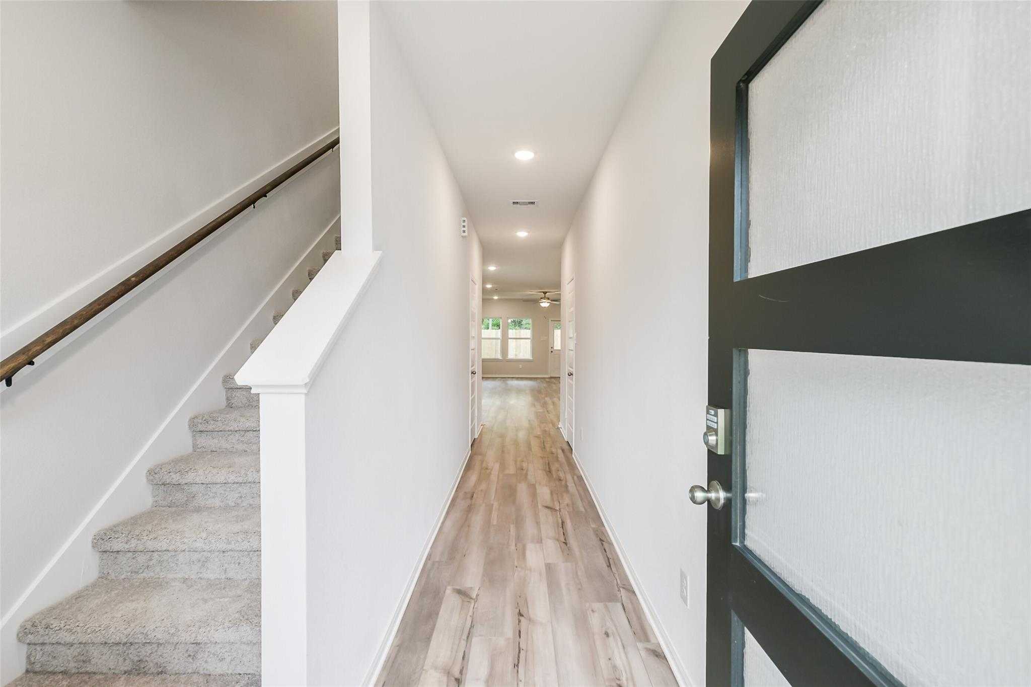 Bright entry hallway with carpeted staircase, hardwood floors, and modern black front door in 5-bedroom Davidson Homes The Brazos F, Conroe, Texas