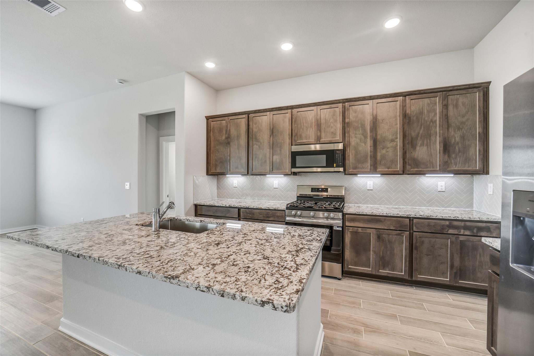 Modern kitchen featuring granite island, shaker cabinets, subway tile backsplash, and stainless appliances in Davidson Homes The Acadia C, Magnolia TX