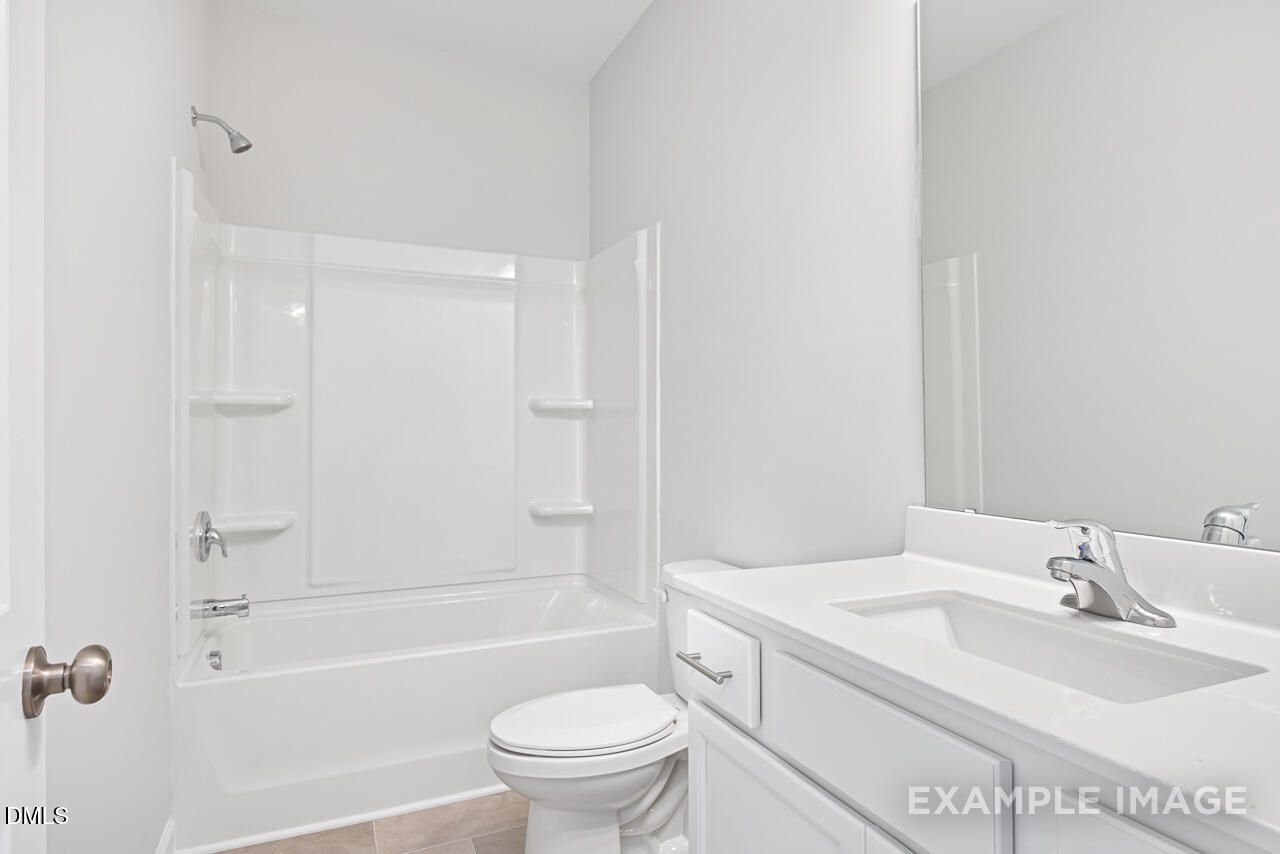 Modern white secondary bathroom with tub-shower combo, vanity sink, and mirror in The Daphne C by Davidson Homes, Lillington, NC
