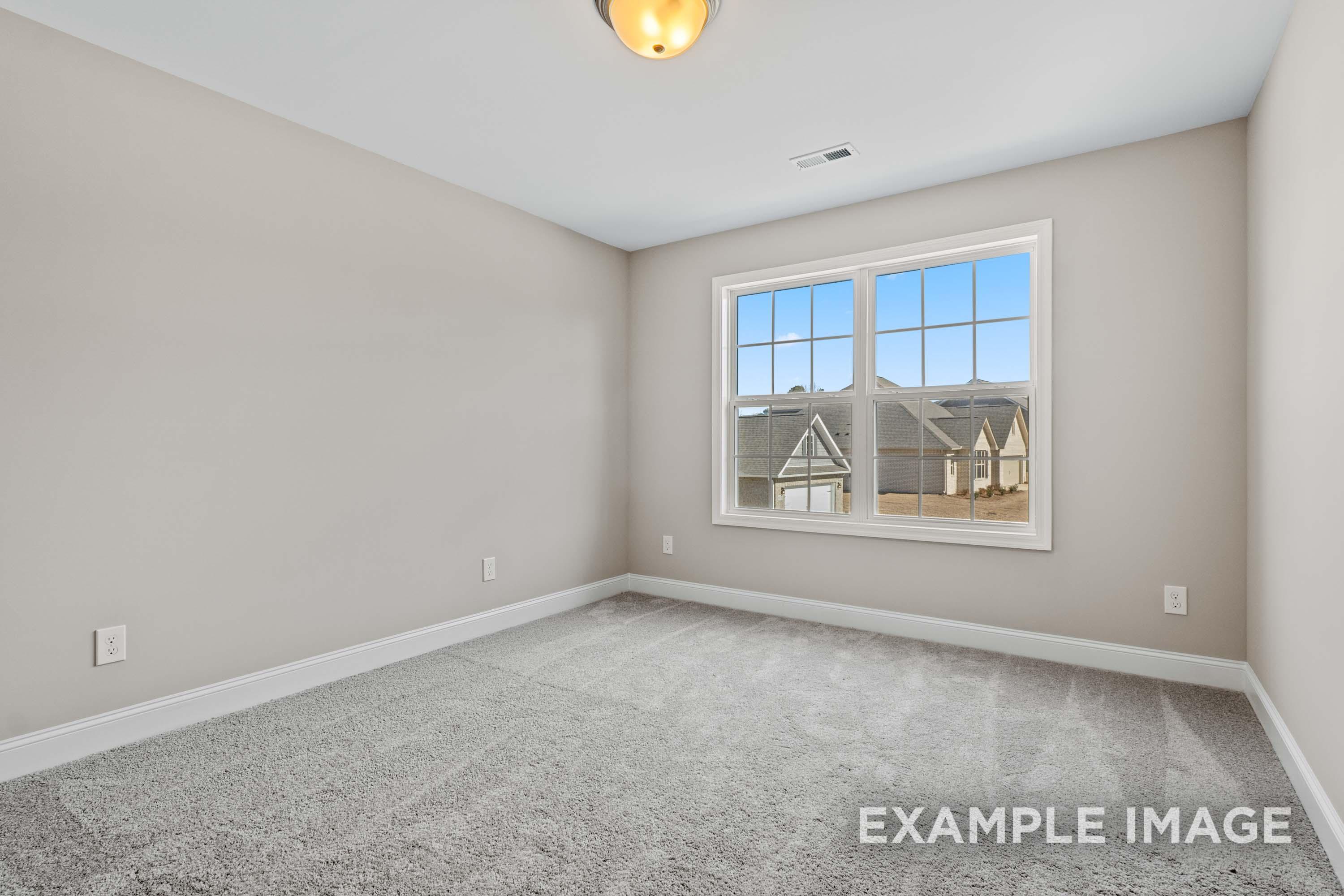 Spacious upper-floor bedroom in The Madison B Davidson Homes design with neutral gray walls, carpet, and large window overlooking neighborhood