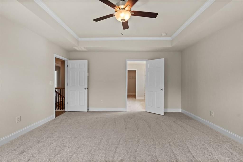 Spacious bedroom with ceiling fan, beige walls, carpeted floor, and double doors to balcony in Davidson Homes The Hickory B at Wehunt Meadows, Hoschton