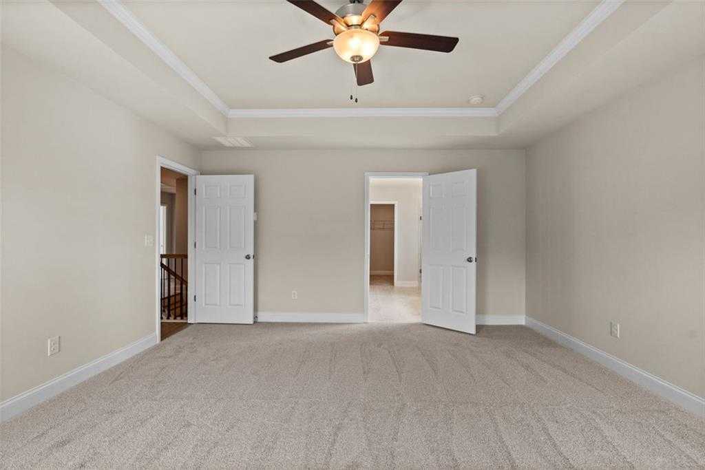 Spacious bedroom with ceiling fan, beige walls, carpeted floor, and double doors to balcony in Davidson Homes The Hickory B at Wehunt Meadows, Hoschton