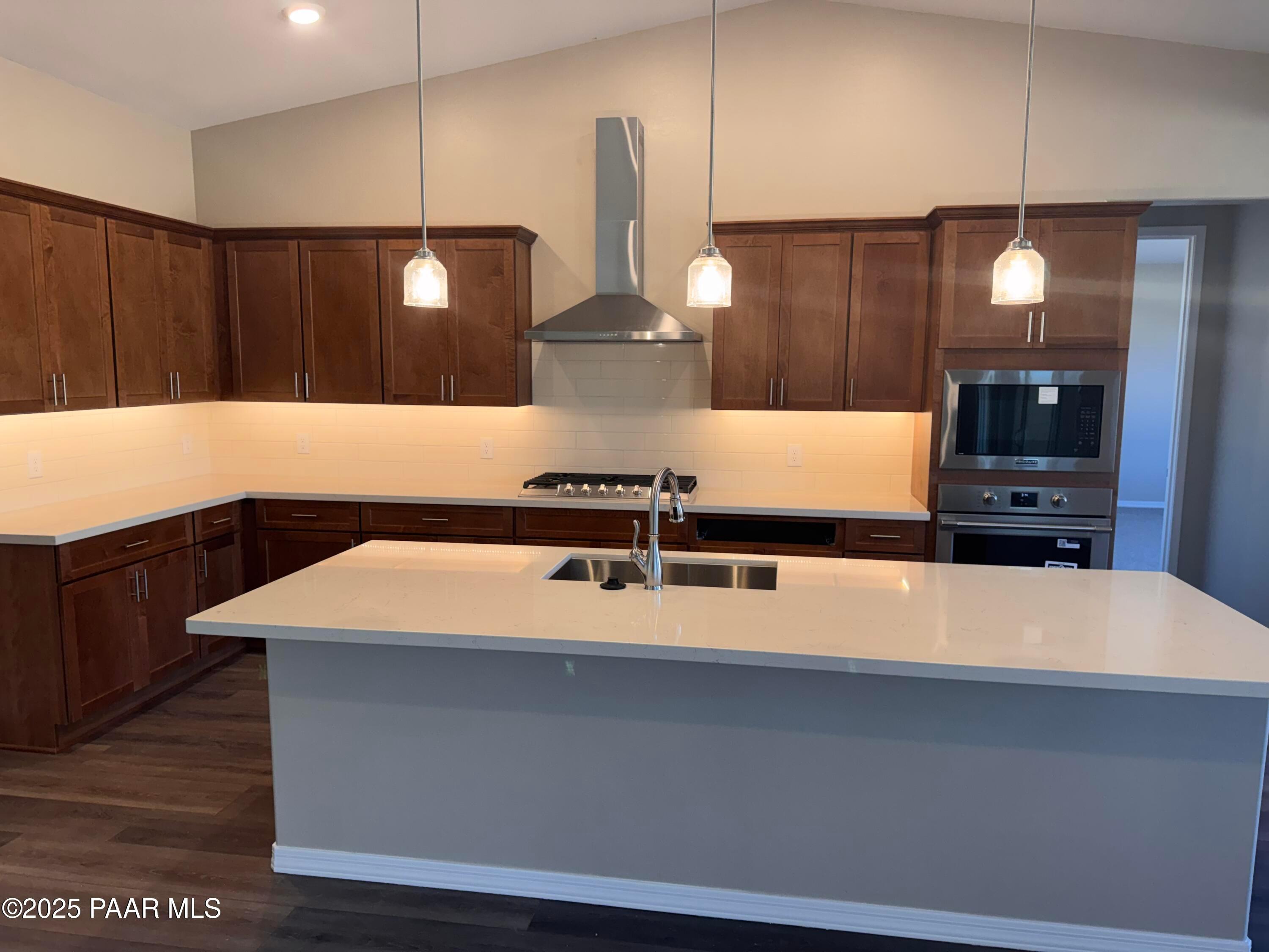 Modern kitchen with white quartz counters, warm wood cabinets, stainless steel appliances, and pendant-lit island in Prescott, AZ home