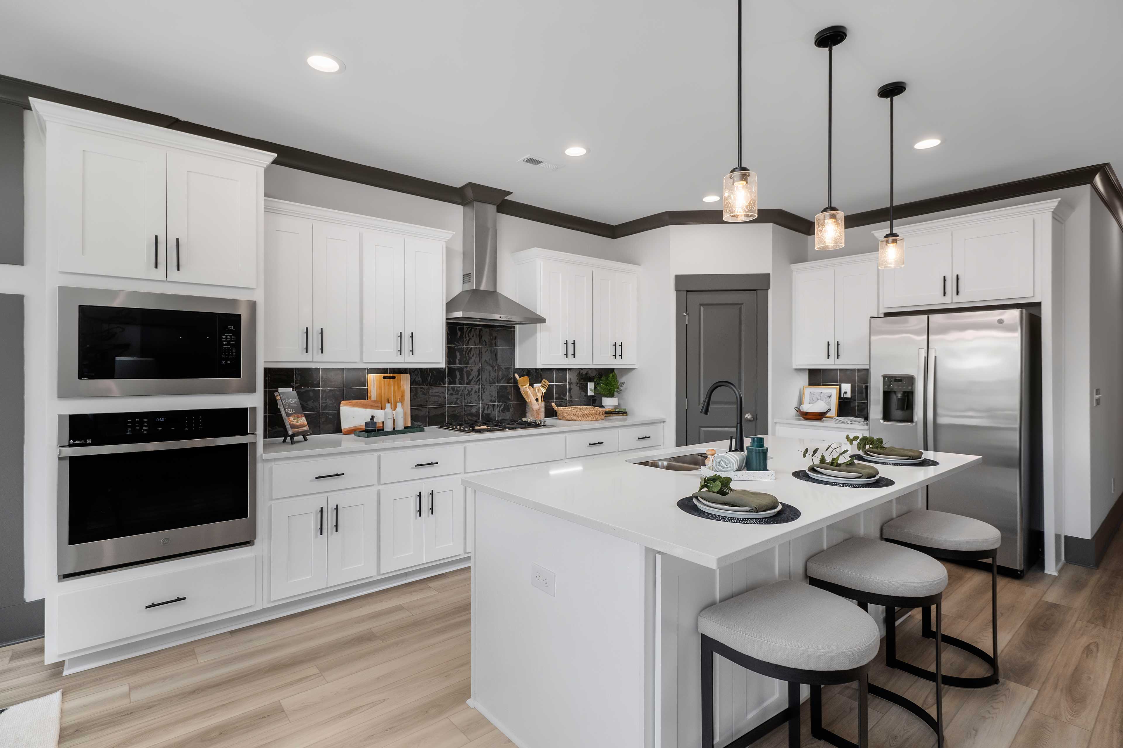 Modern white kitchen at Barnett's Crossing in Madison AL with large island, bar stools, stainless appliances, hardwood floors