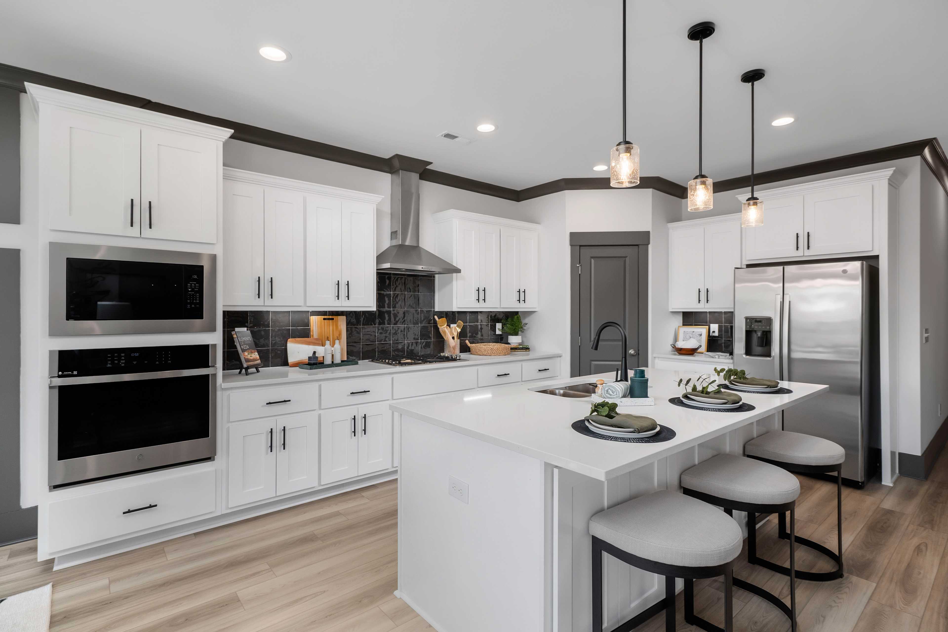 Modern white kitchen at Barnett's Crossing in Madison AL with large island, bar stools, stainless appliances, hardwood floors
