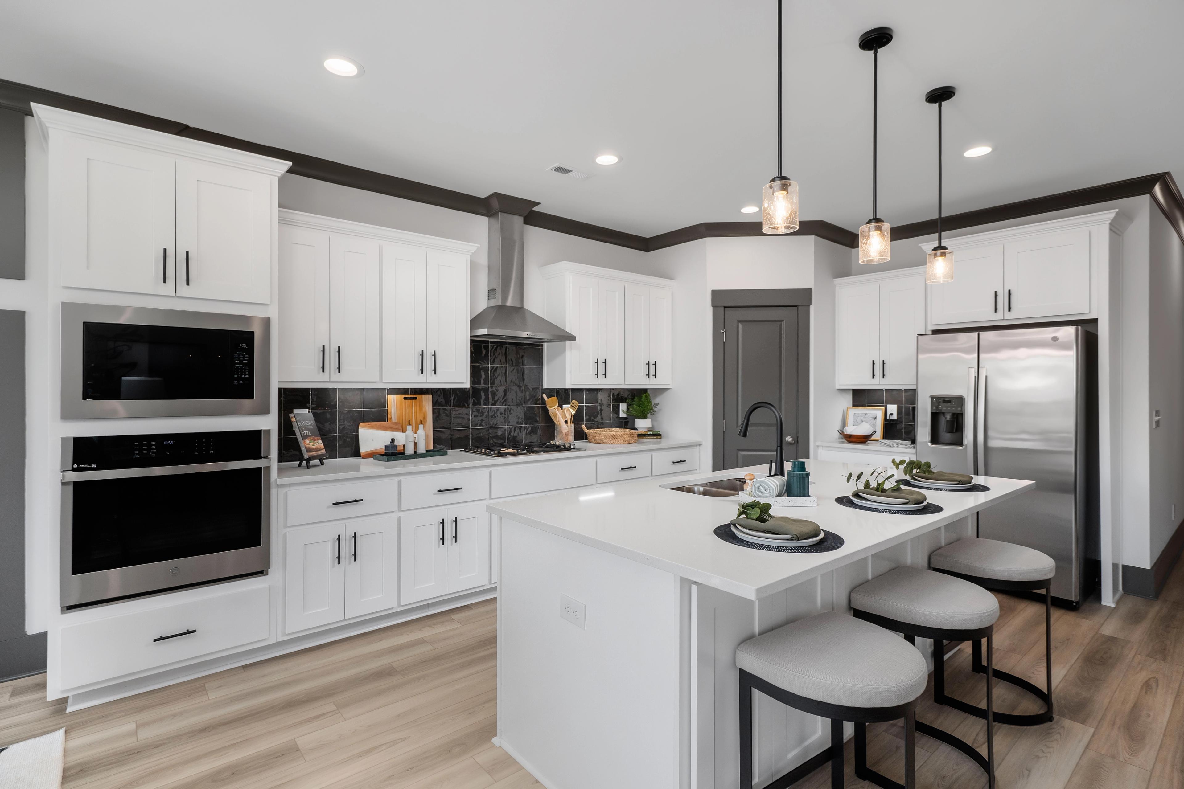 Modern white kitchen at Barnett's Crossing in Madison AL with large island, bar stools, stainless appliances, hardwood floors