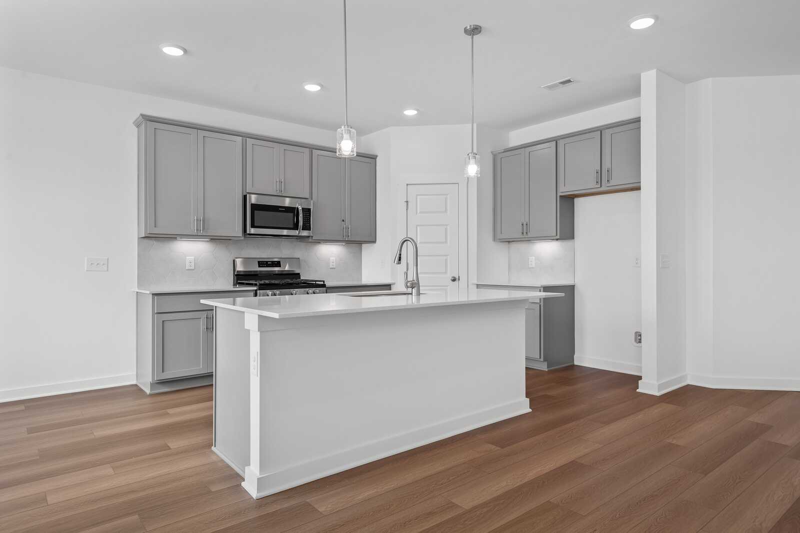 Spacious modern kitchen in The Asheville featuring gray shaker cabinets, white quartz island, stainless steel appliances, and hardwood floors