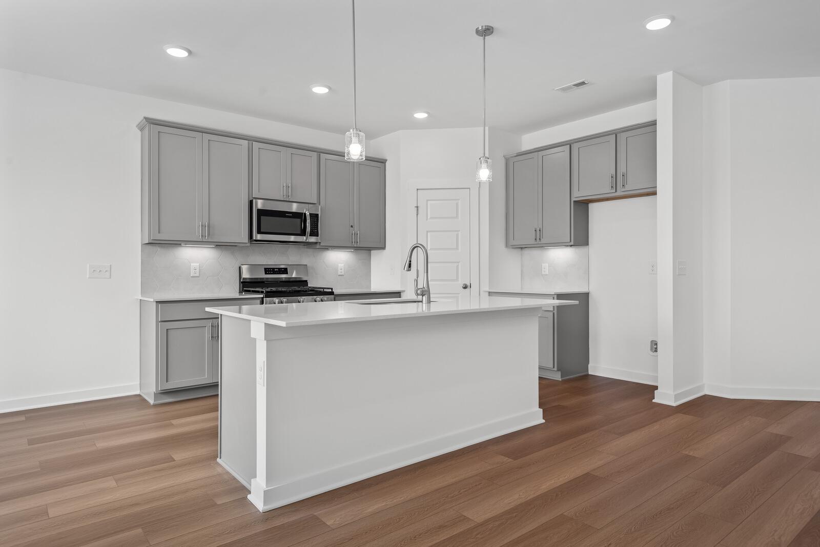 Spacious modern kitchen in The Asheville with gray shaker cabinets, white quartz island, stainless steel appliances, pendant lights, hardwood floors
