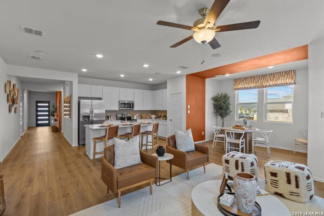 Open-concept kitchen and living area with stainless appliances, white cabinets, leather seating, and wooden floors in Davidson Homes The Daphne H, Seguin, Texas