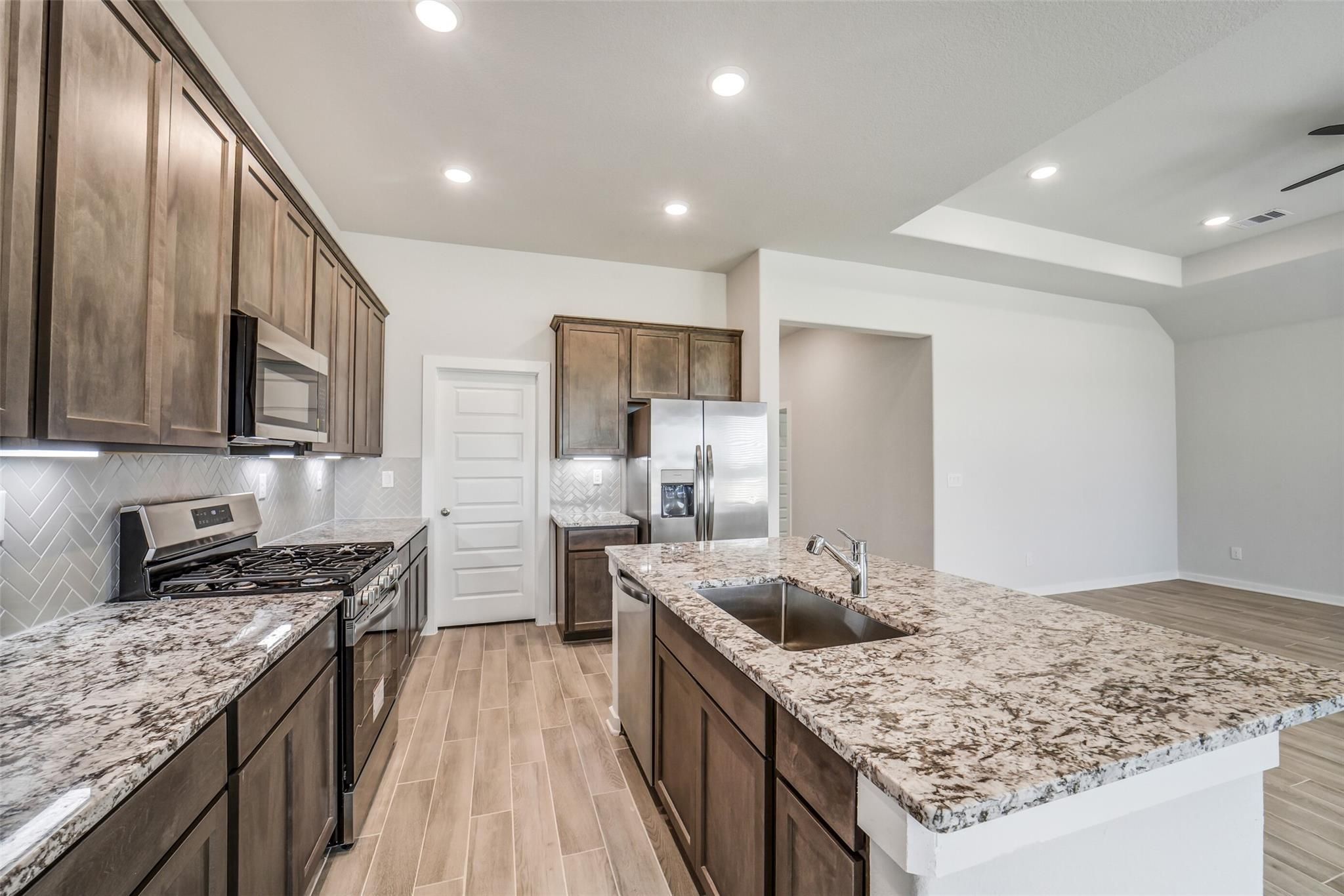Modern open-concept kitchen with granite countertops, stainless steel appliances, subway tile backsplash, and central island in Davidson Homes The Acadia C, Magnolia TX