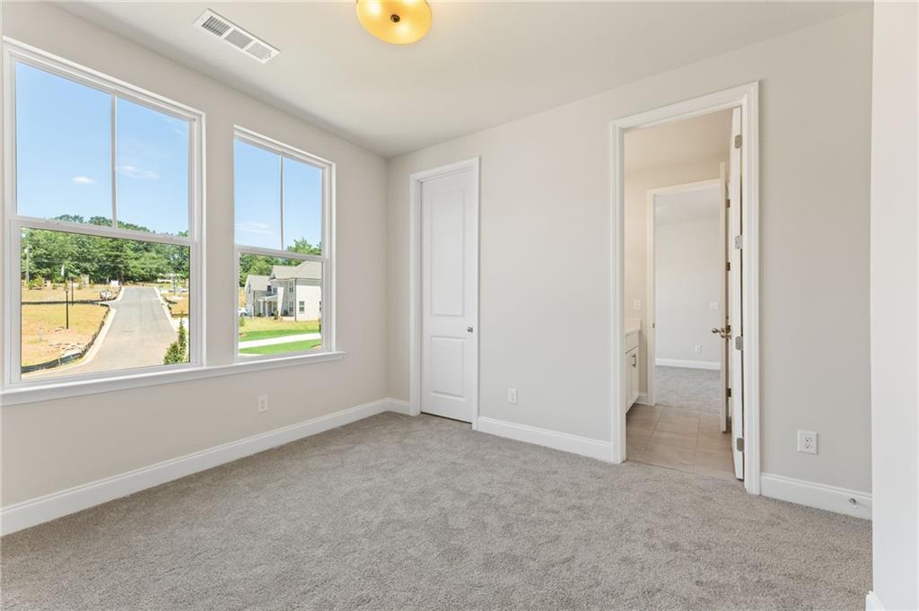 Spacious bedroom with large windows overlooking neighborhood, attached bath, and beige walls in Davidson Homes Danbury C, Buford, GA