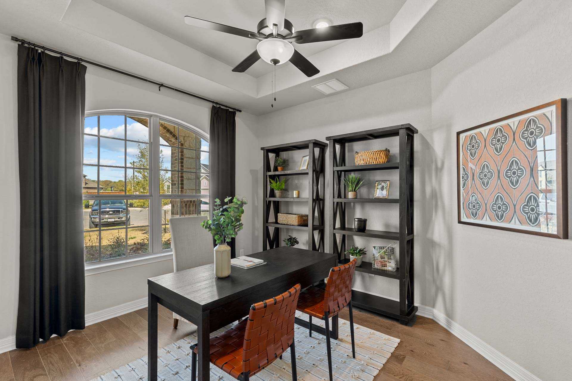Spacious study room in The Summerlin B home with black desk, leather chairs, bookshelves, arched window, and plants
