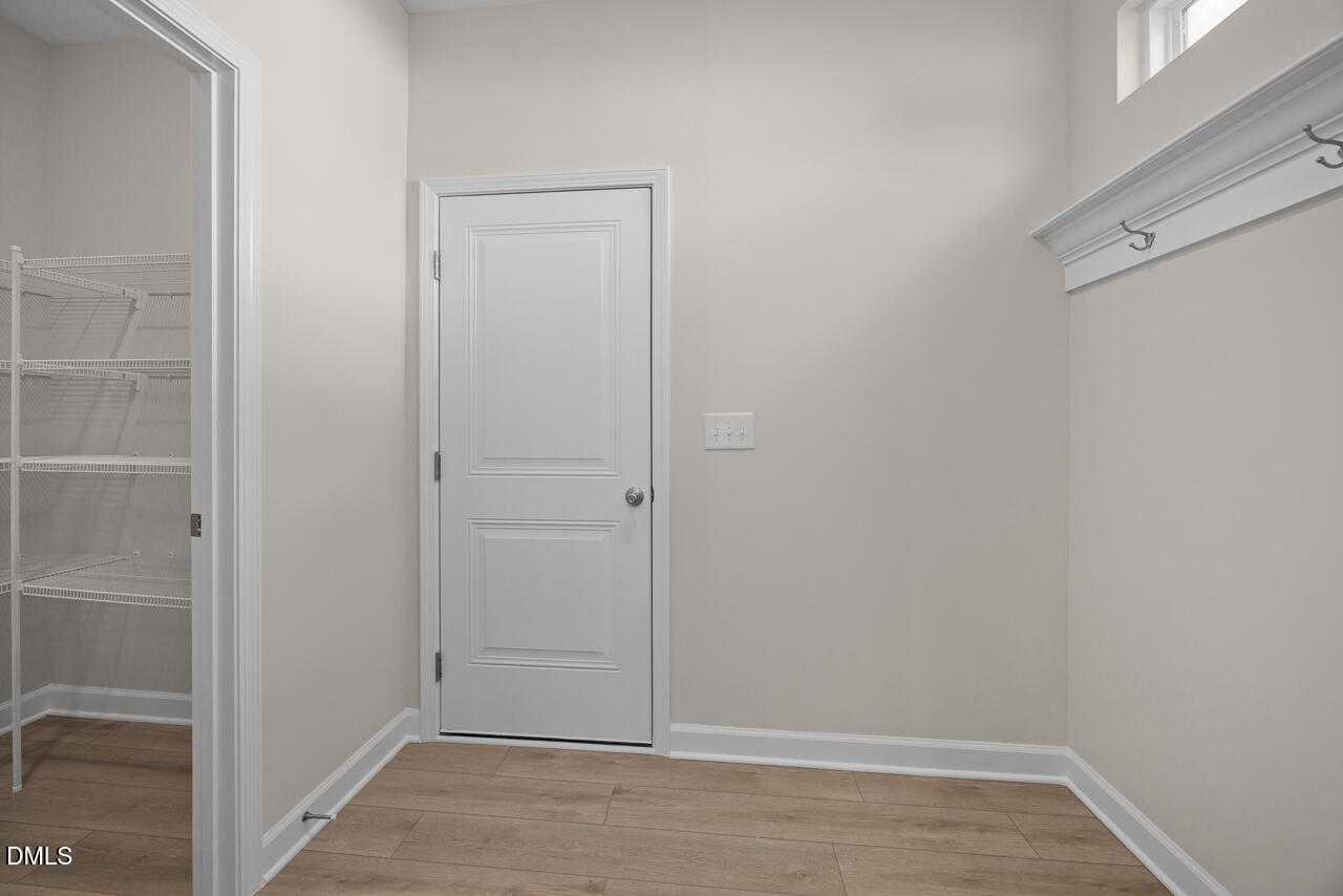 Functional mudroom with built-in white shelves, coat hooks, and doors on hardwood floors in Davidson Homes The Gavin C, Lillington, NC