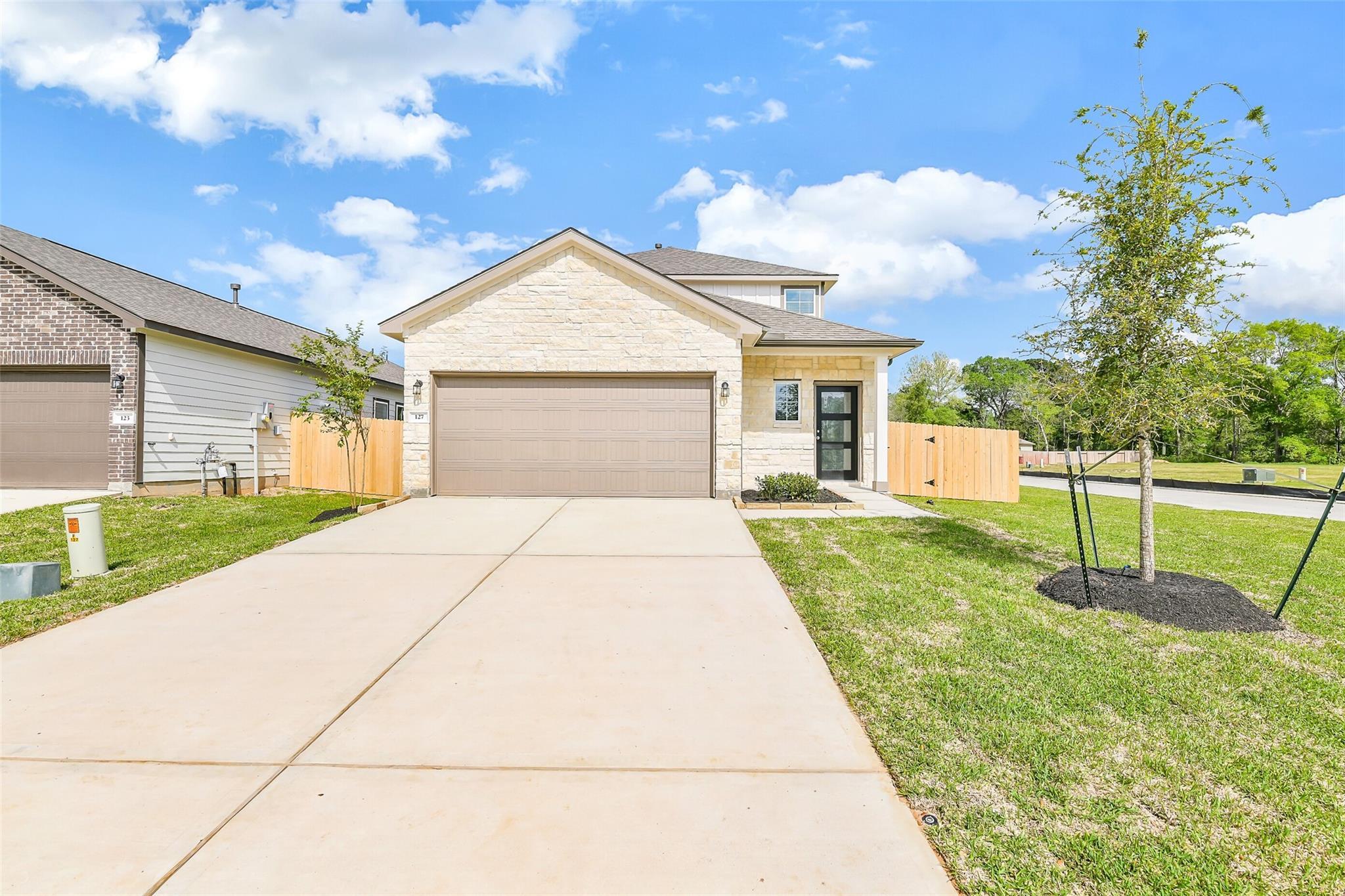 Modern two-story San Marcos E home with beige stone facade, two-car garage, concrete driveway, and front yard in Conroe, Texas