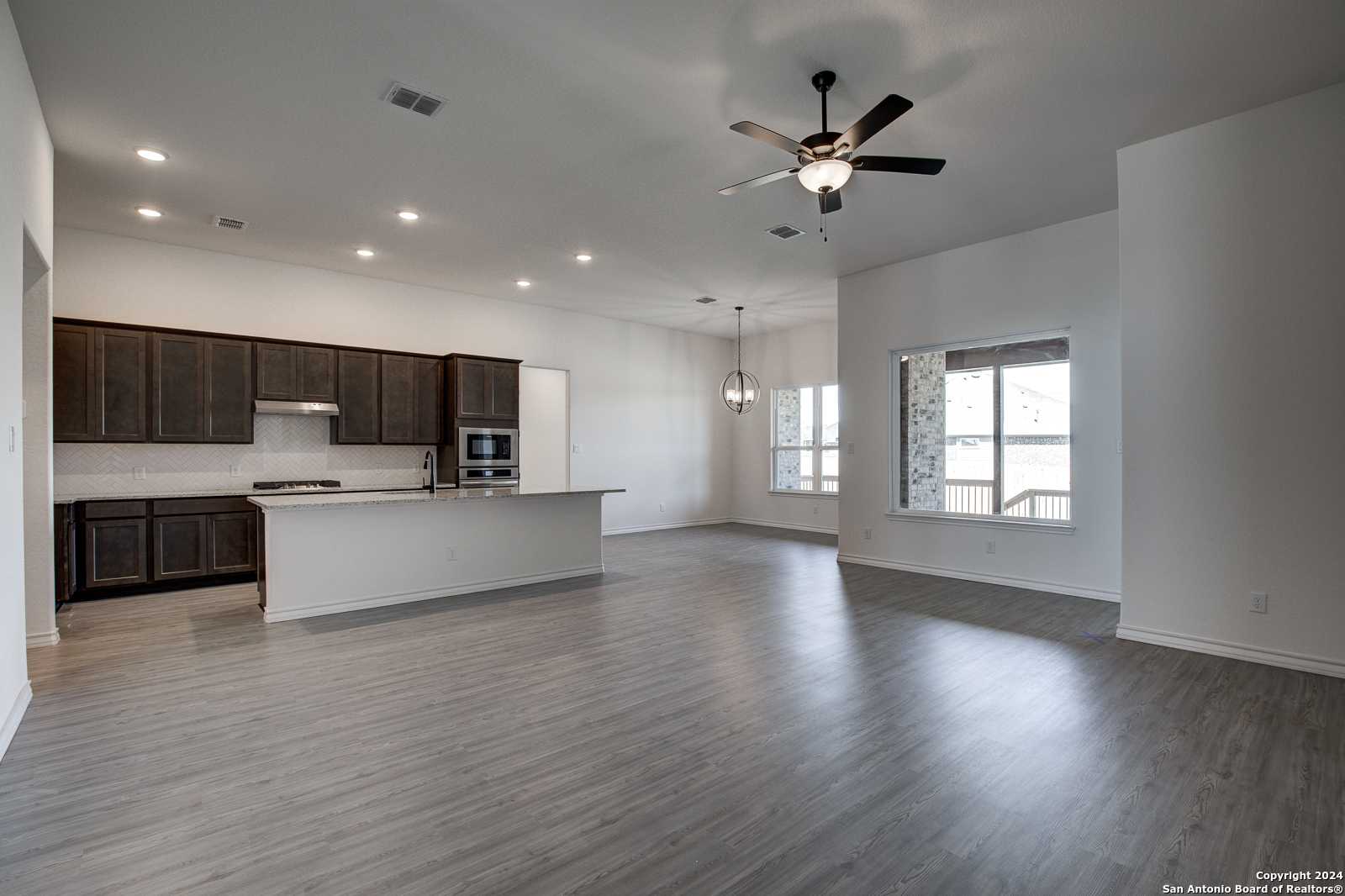 Modern open-concept kitchen with dark shaker cabinets, white island, and ceiling fans in The Garner B home, Castroville, Texas