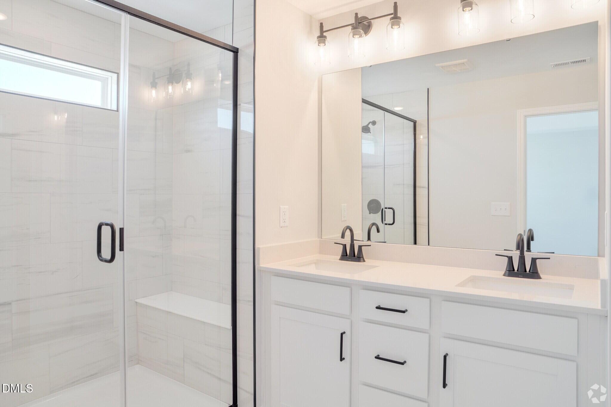 Modern white master bathroom with dual vanities, matte black fixtures, and walk-in tile shower in Davidson Homes The Mitchell, Knightdale NC