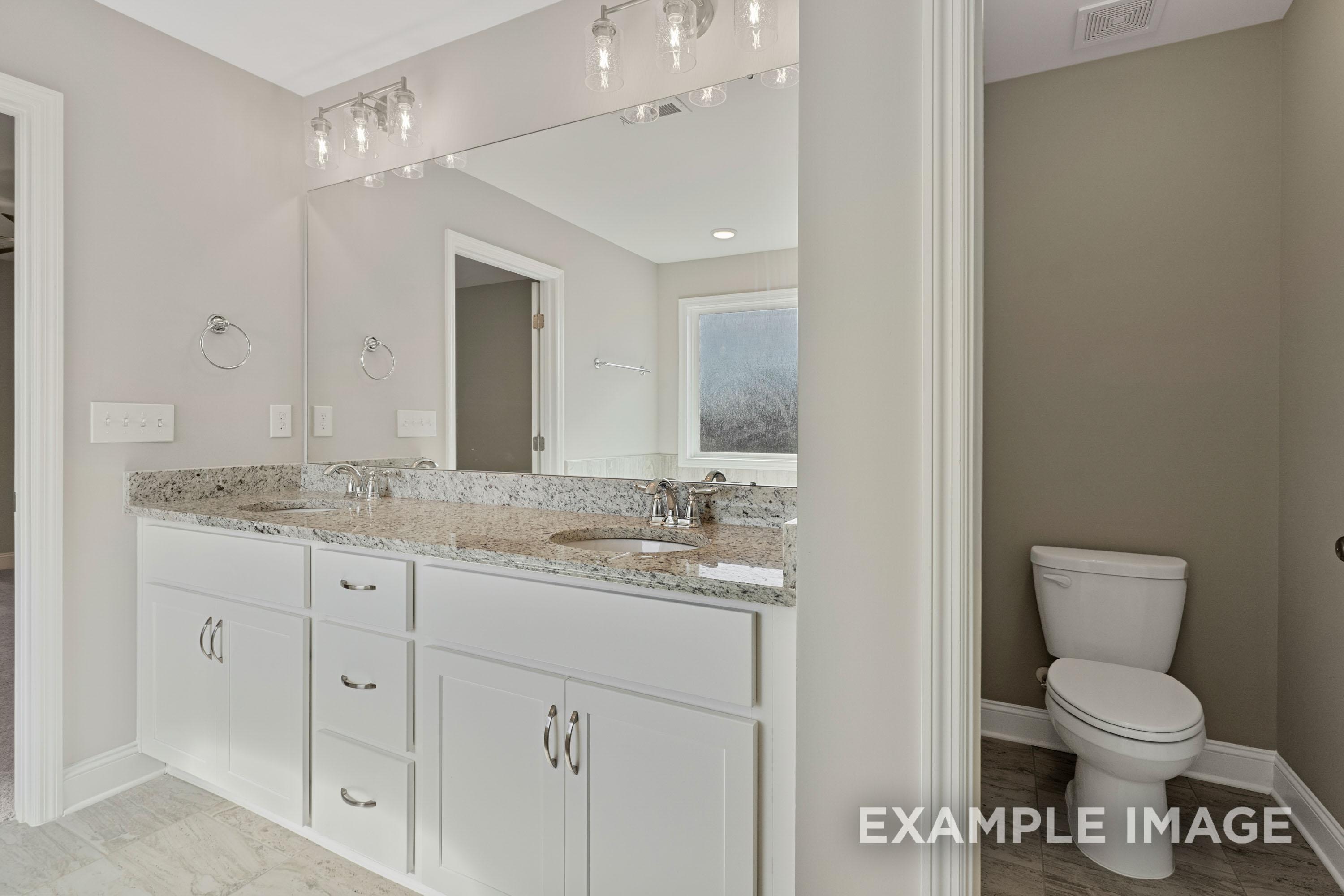 Spacious master bathroom in The Madison B featuring double granite vanity, white cabinets, large mirror, and separate toilet area